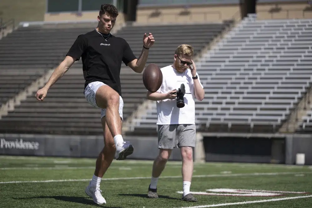 Adam Botkin, a football TikTok influencer, punts the ball while recording a video for a post with Brandin Evans, right, at Washington-Grizzly Stadium in Missoula, Mont., on Monday, May 1. Botkin, a former walk-on place kicker and punter for the Montana Grizzlies, gained notoriety on the social media platform after videos of him performing kicking tricks went viral.