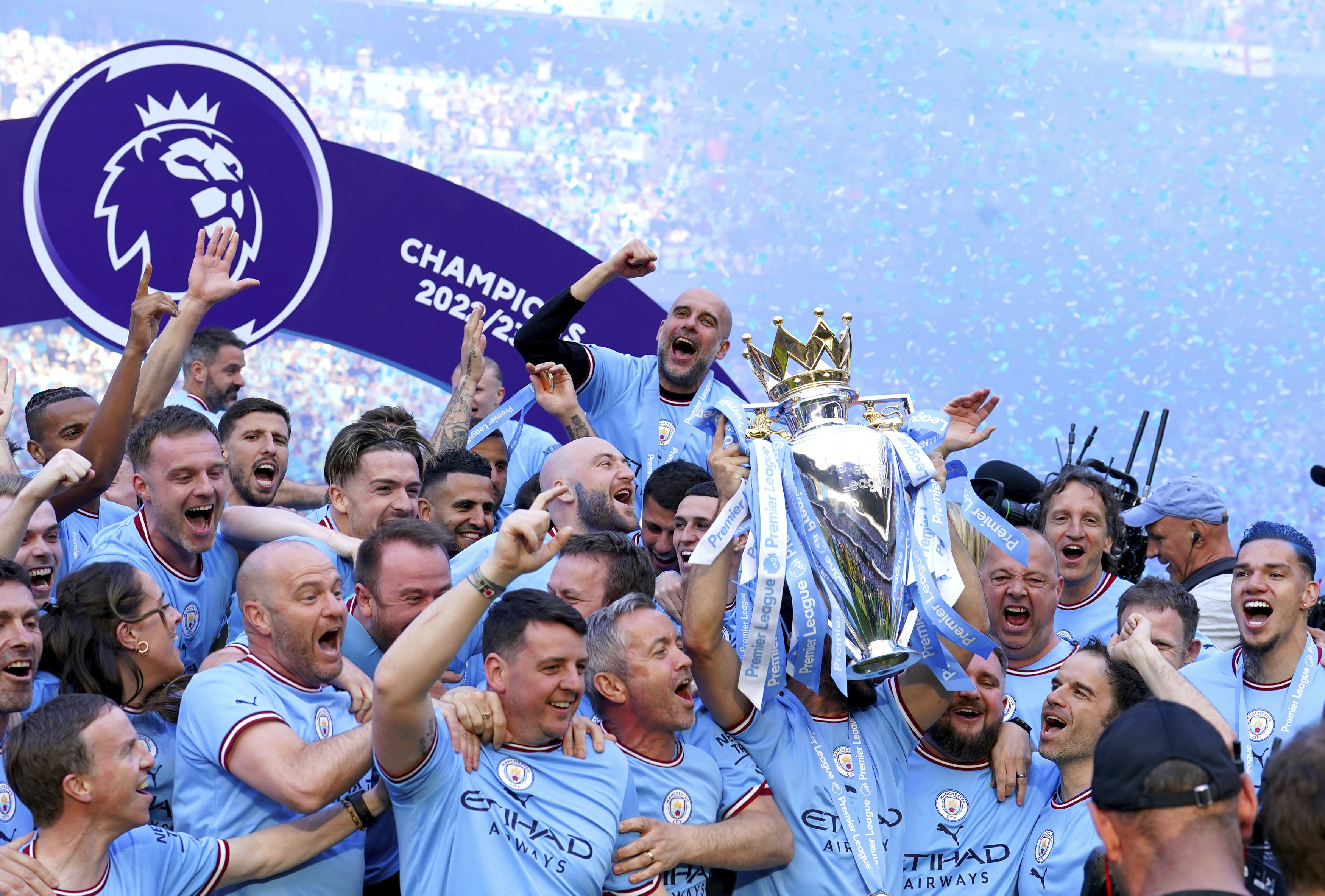 Manchester City players and staff including Pep Guardiola celebrate with the Premier League trophy after their English Premier League title win at the end of the English Premier League soccer match between Manchester City and Chelsea at the Etihad Stadium in Manchester, England, Sunday, May 21, 2023. 