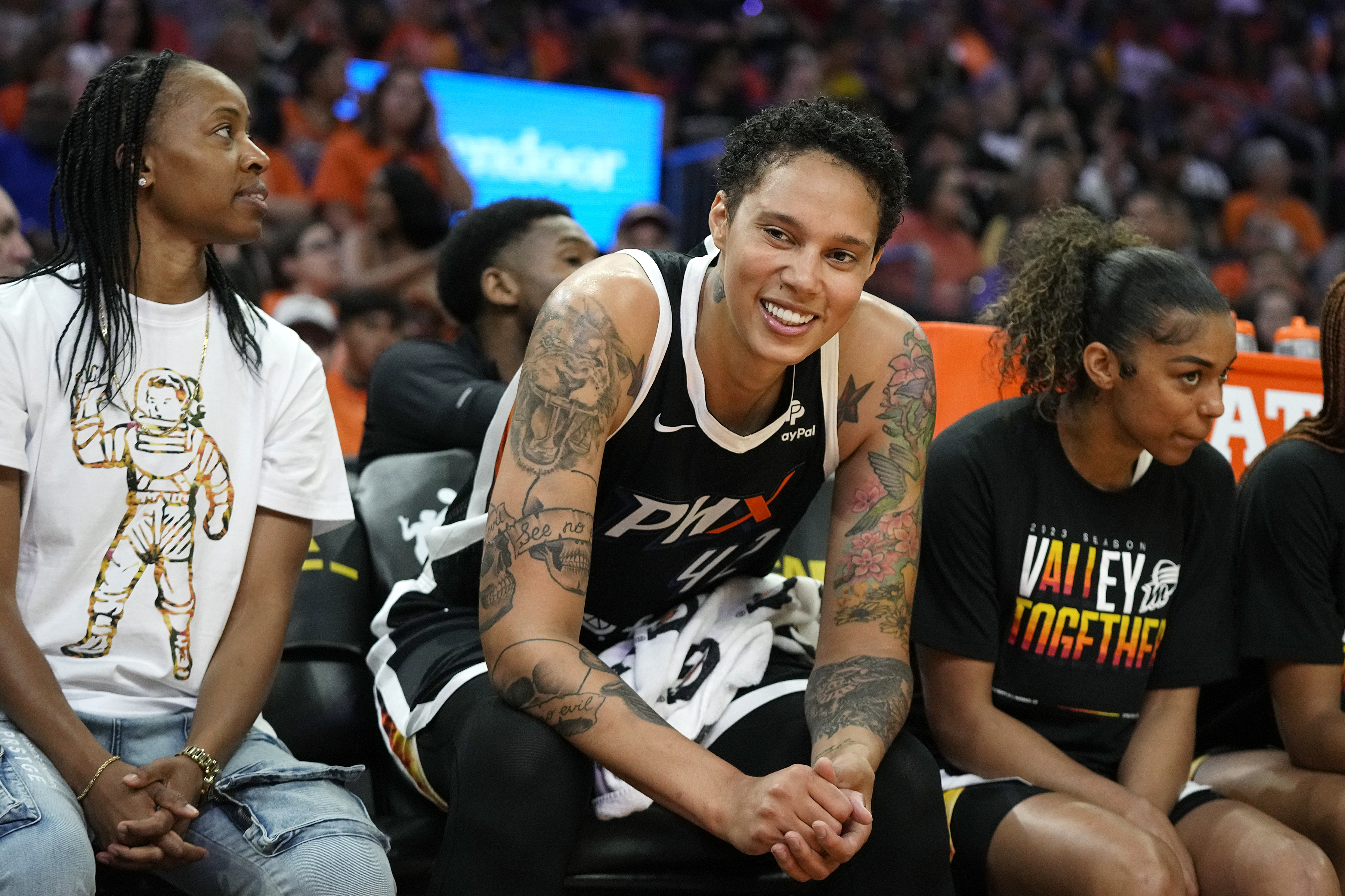 Phoenix Mercury center Brittney Griner smiles at the fans as she sits between Mercury's Shey Peddy, left, and Evina Westbrook, right, during the first half of a WNBA basketball game against the Chicago Sky, Sunday, May 21, 2023, in Phoenix. 