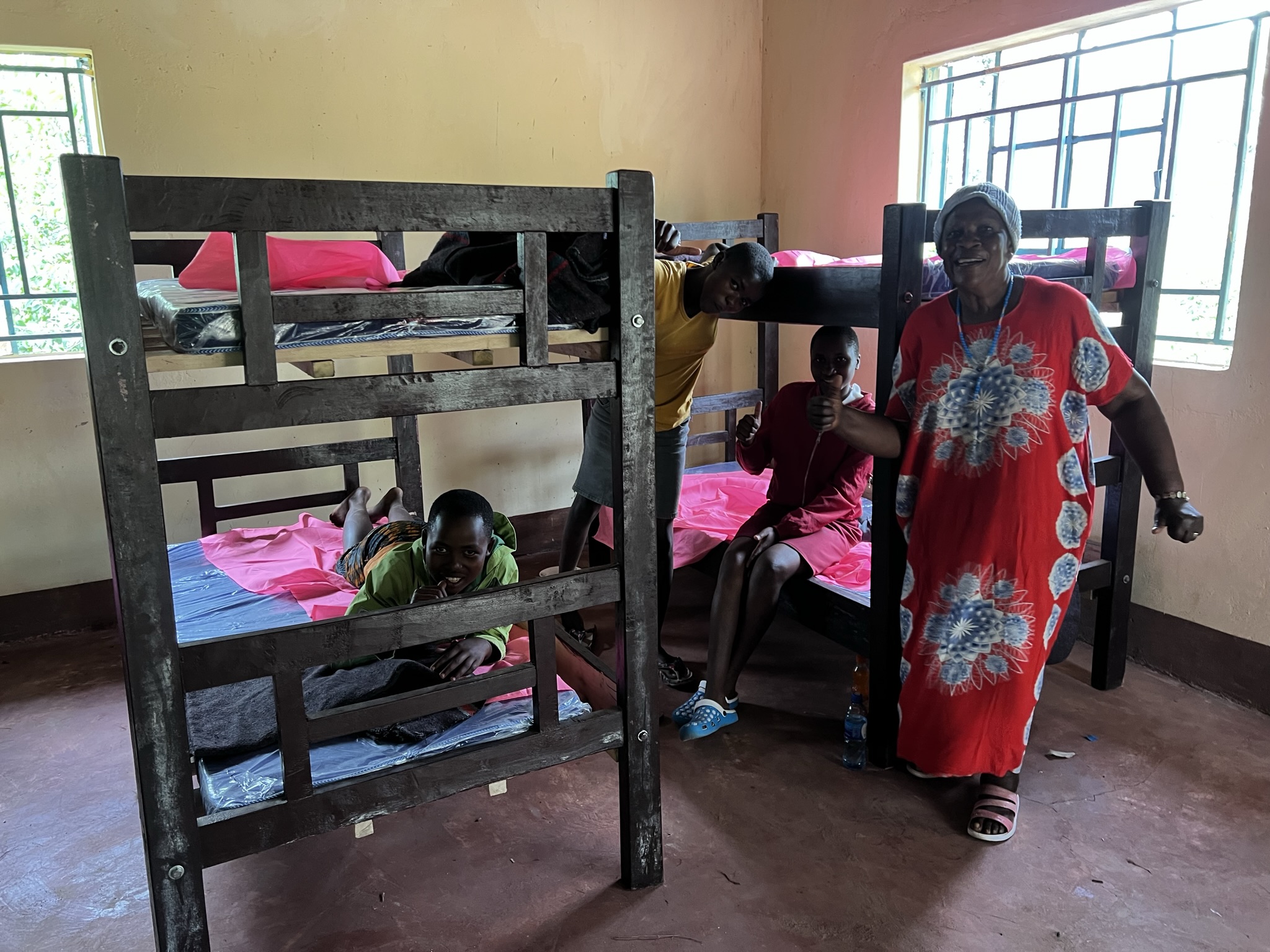 A volunteer and kids at a rescue center in Kuria, Migori County, Kenya, are happy about receiving beds donated by WHOlives. This ensures girls who are escaping violence have a safe place to sleep.