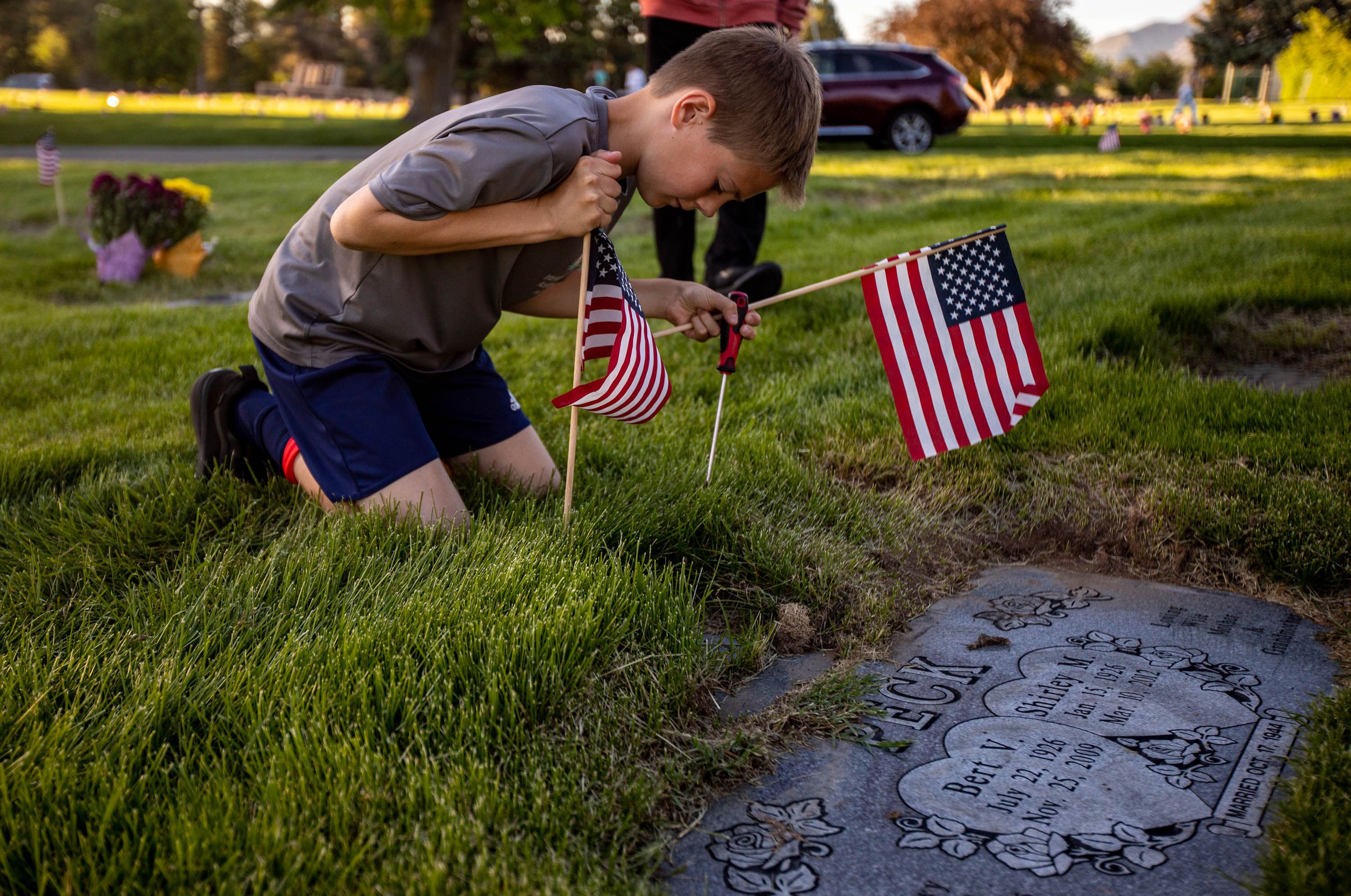 Volunteer Tate Cocciniglio, 11, places a flag at a marker at Larkin Sunset Gardens Cemetery in Sandy on Thursday, May 27, 2021. More than 200 youth volunteers from around the Salt Lake Valley honored military veterans for Memorial Day by placing 3,000 American flags on the graves of service members. In addition, they swept and polished headstones and helped beautify cemetery grounds.