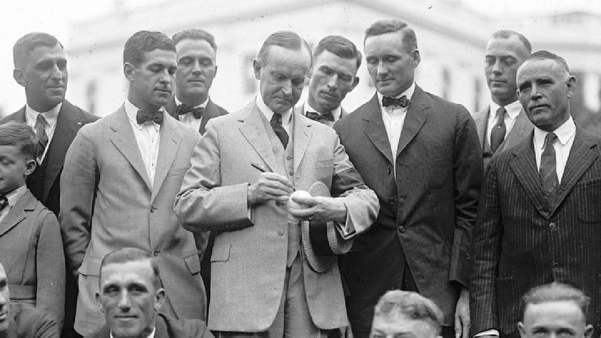 President Calvin Coolidge signs a baseball for Hall of Fame pitcher Walter Johnson as other members of the Senators look on in 1924.