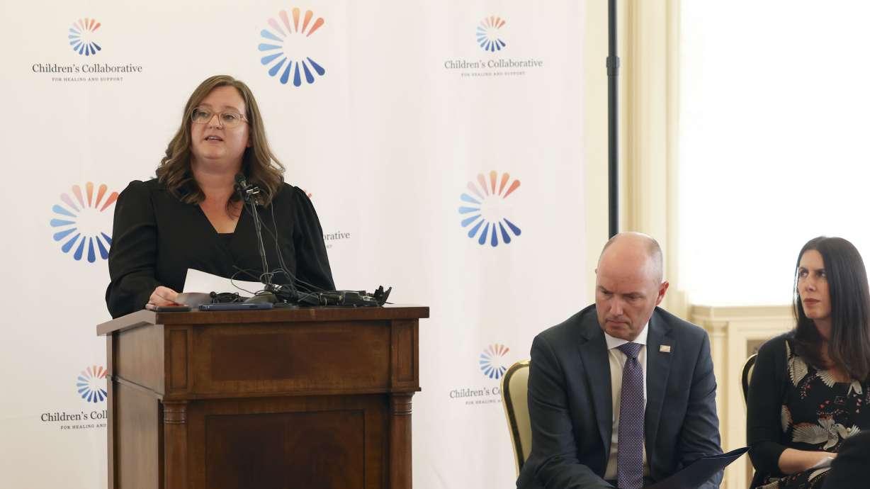 Candalyn Mettmann speaks of a new initiative that supports grieving children and boosts access to services in Salt Lake City on Thursday. Gov. Spencer Cox listens with Heather Nesle, president of the New York Life Foundation.