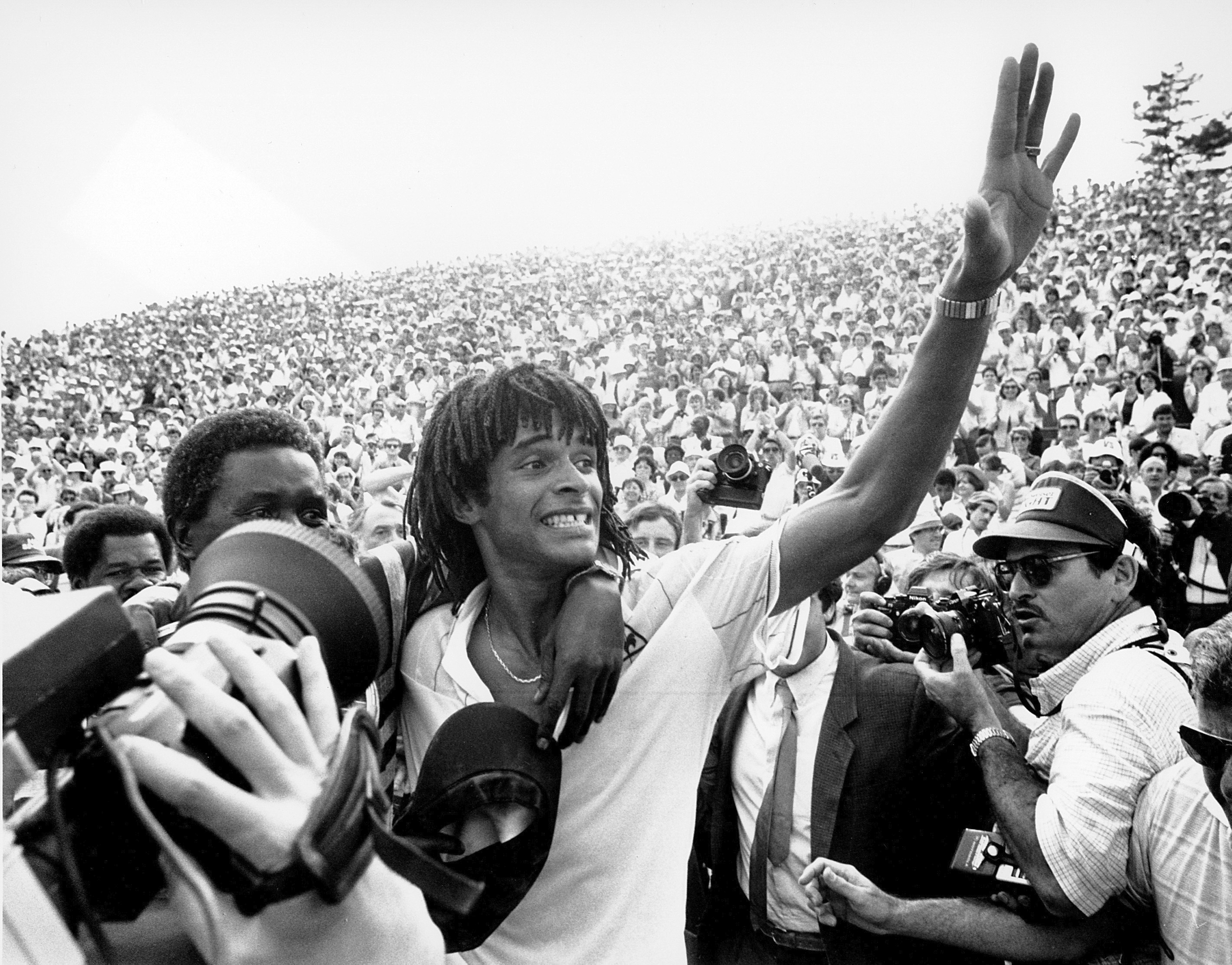 FILE - Yannick Noah, of France, waves to the crowd at Roland Garros stadium in Paris after defeating Sweden's Mats Wilander to win the French Open men's singles tennis title, June 5, 1983. Obscured at left hugging Yannick Noah is his father. . 