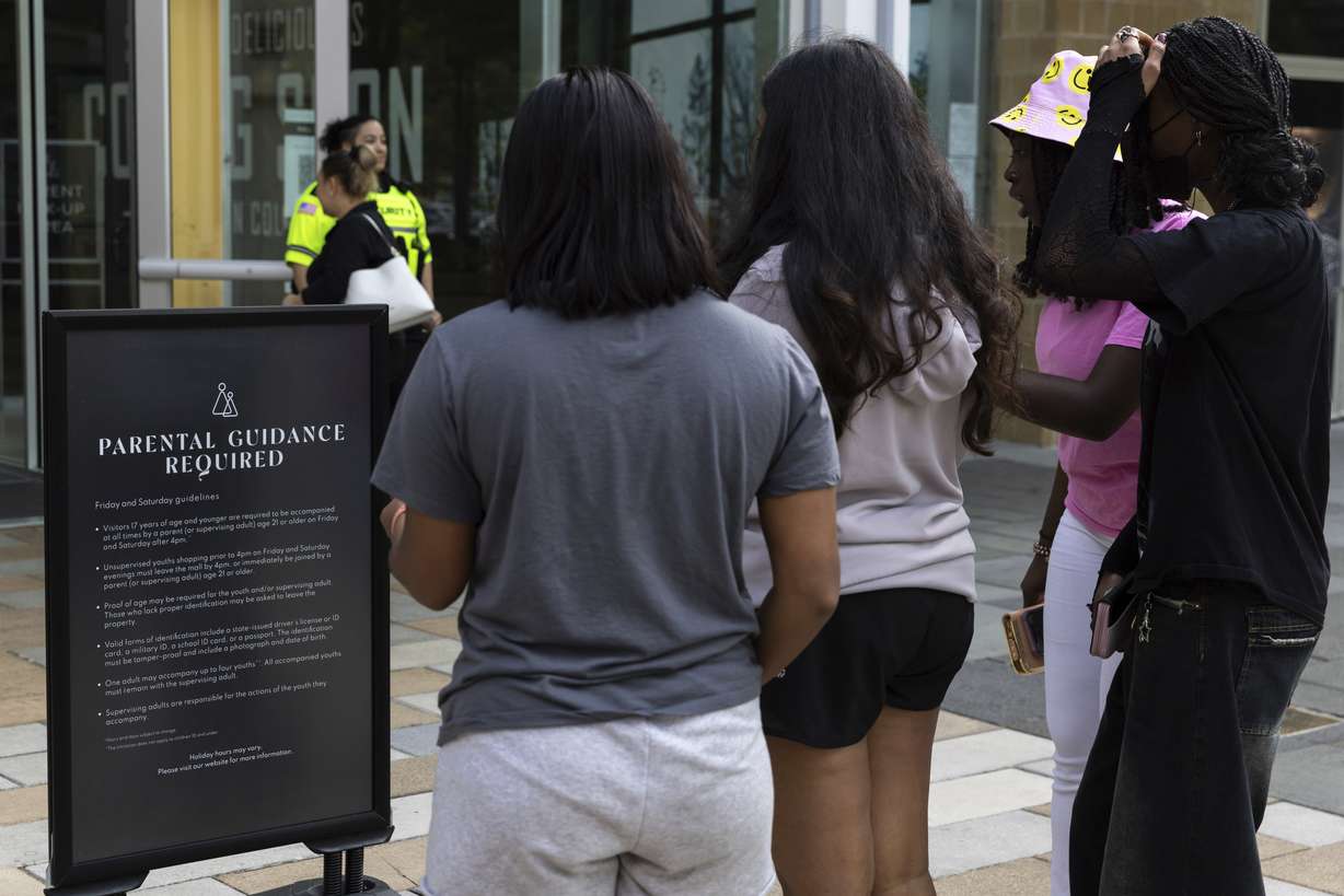 A security guard stands by as teens read a sign explaining the Mall in Columbia's "Parental Guidance Required" program May 12, 2023, in Columbia, Md. The program requires that all visitors under 18 be accompanied by an adult who is at least 21-years-old after 4 p.m. on Fridays and Saturdays.