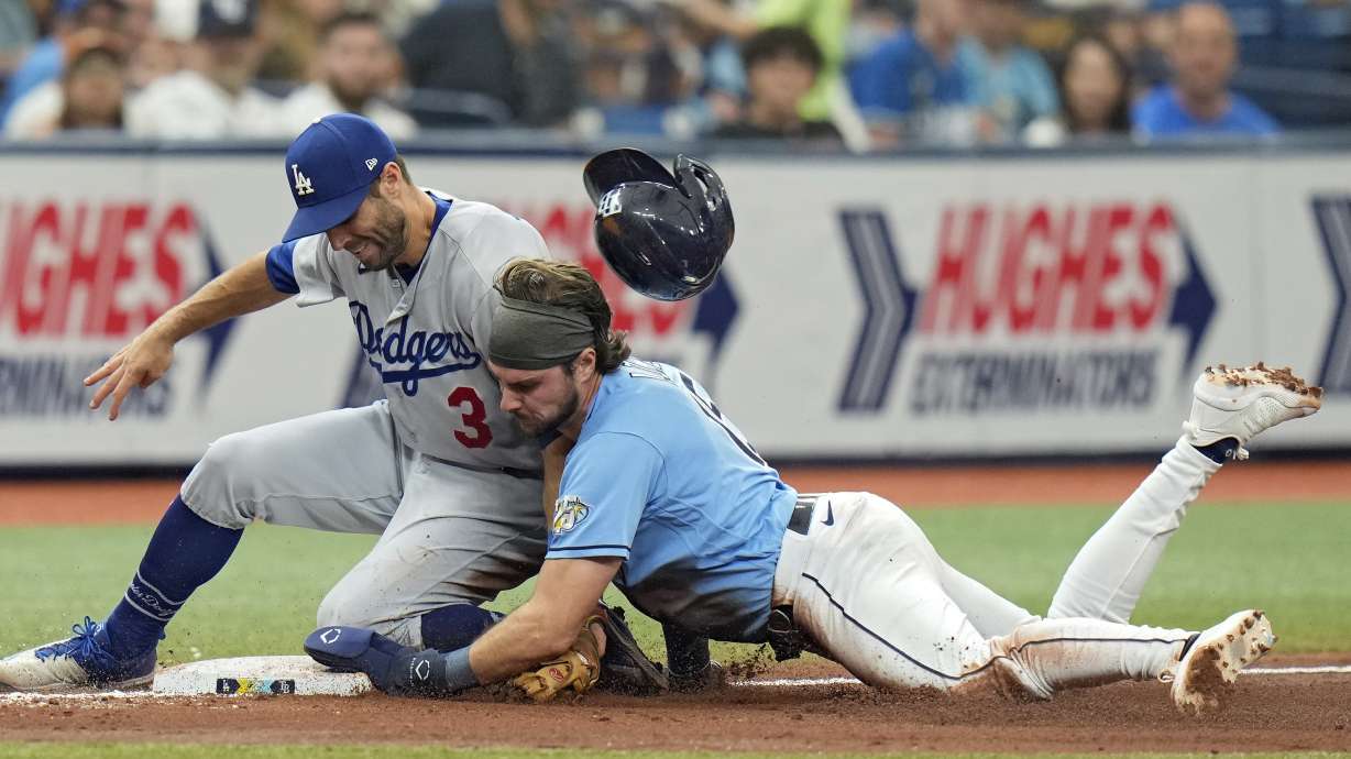 Tampa Bay Rays' Josh Lowe loses his helmet as he steals third base ahead of the tag by Los Angeles Dodgers' Chris Taylor (3) during the fourth inning of a baseball game Sunday, May 28, 2023, in St. Petersburg, Fla.
