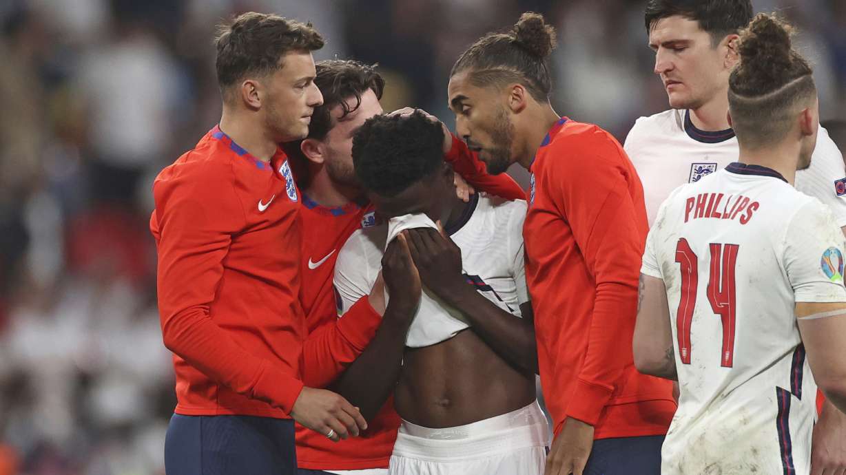 FILE - England players comfort teammate Bukayo Saka after he failed to score a penalty during a penalty shootout after extra time during of the Euro 2020 soccer championship final match between England and Italy at Wembley stadium in London, Sunday, July 11, 2021. Missing penalties in a major international soccer final was bad enough for three Black players, Marcus Rashford, Jadon Sancho and Bukayo Saka, who were on England's national team. Being subjected to a torrent of racial abuse on social media in the aftermath made it even worse. Saka, who has more than 1 million followers on Twitter, remains on social media despite the abuse after England's Euro 2020 loss.