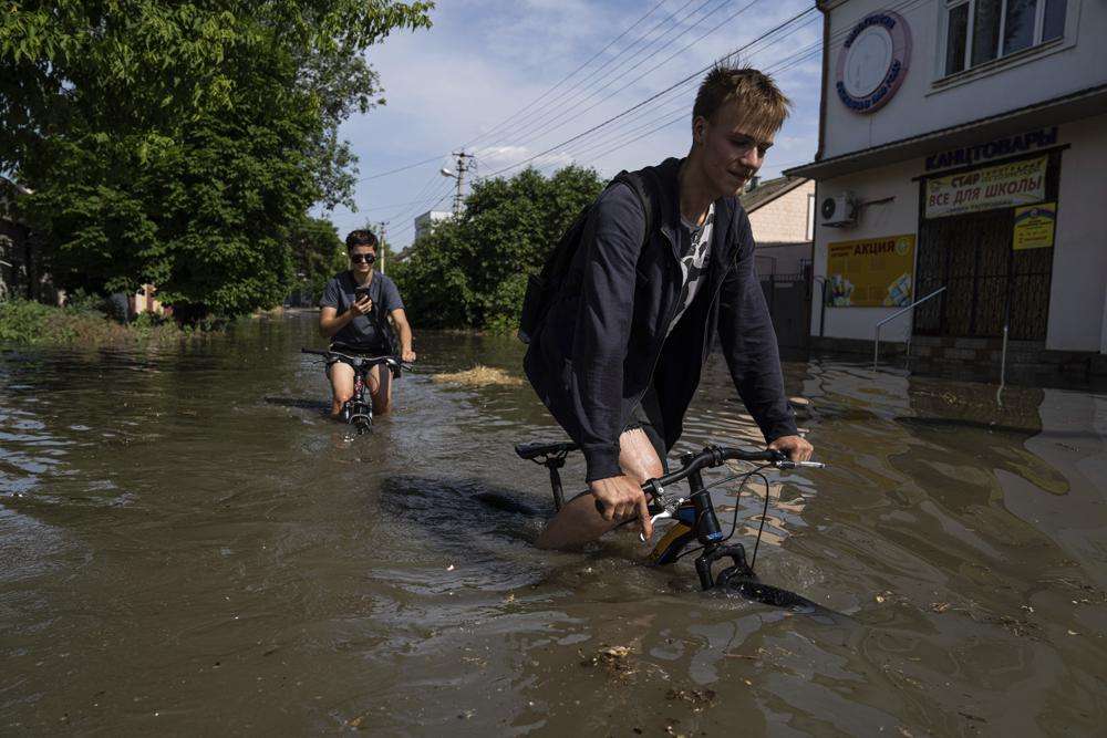 Local residents try to ride their bikes along a flooded road after the Kakhovka dam blew overnight, in Kherson, Ukraine, Tuesday. Ukraine on Tuesday accused Russian forces of blowing up a major dam and hydroelectric power station in a part of southern Ukraine that Russia controls, risking environmental disaster.