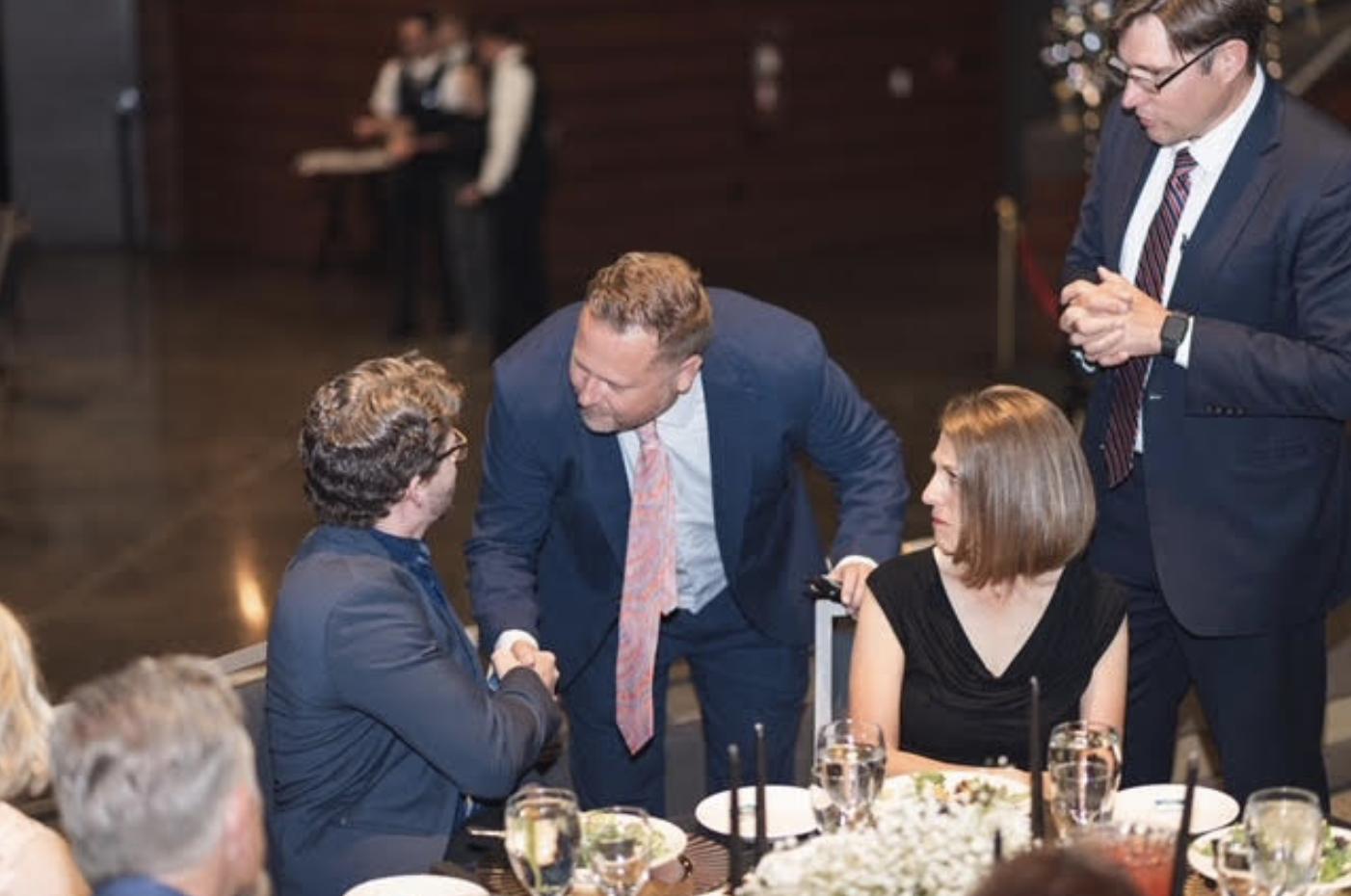 Volcanic Chairman and CEO Jeremy Brockbank shakes hands with seated guests.