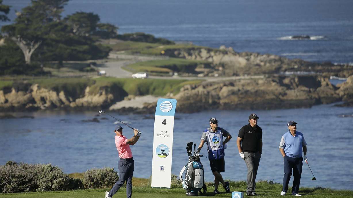 FILE - Rory McIlroy, of Northern Ireland, hits from the fourth tee of the Spyglass Hill Golf Course during the first round of the AT&T Pebble Beach National Pro-Am golf tournament Feb. 8, 2018, in Pebble Beach, Calif. Looking on from left are caddie Tim Mickelson, Phil Mickelson and Jimmy Dunne III. Dunne was instrumental in getting the PGA Tour to meet with the head of Saudi Arabia's wealth fund.