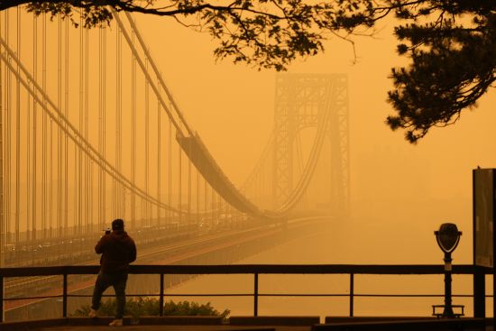 A man talks on his phone as he looks through the haze at the George Washington Bridge from Fort Lee, N.J., Wednesday. Intense Canadian wildfires are blanketing the northeastern U.S. in a dystopian haze, turning the air acrid, the sky yellowish gray and prompting warnings for vulnerable populations to stay inside.