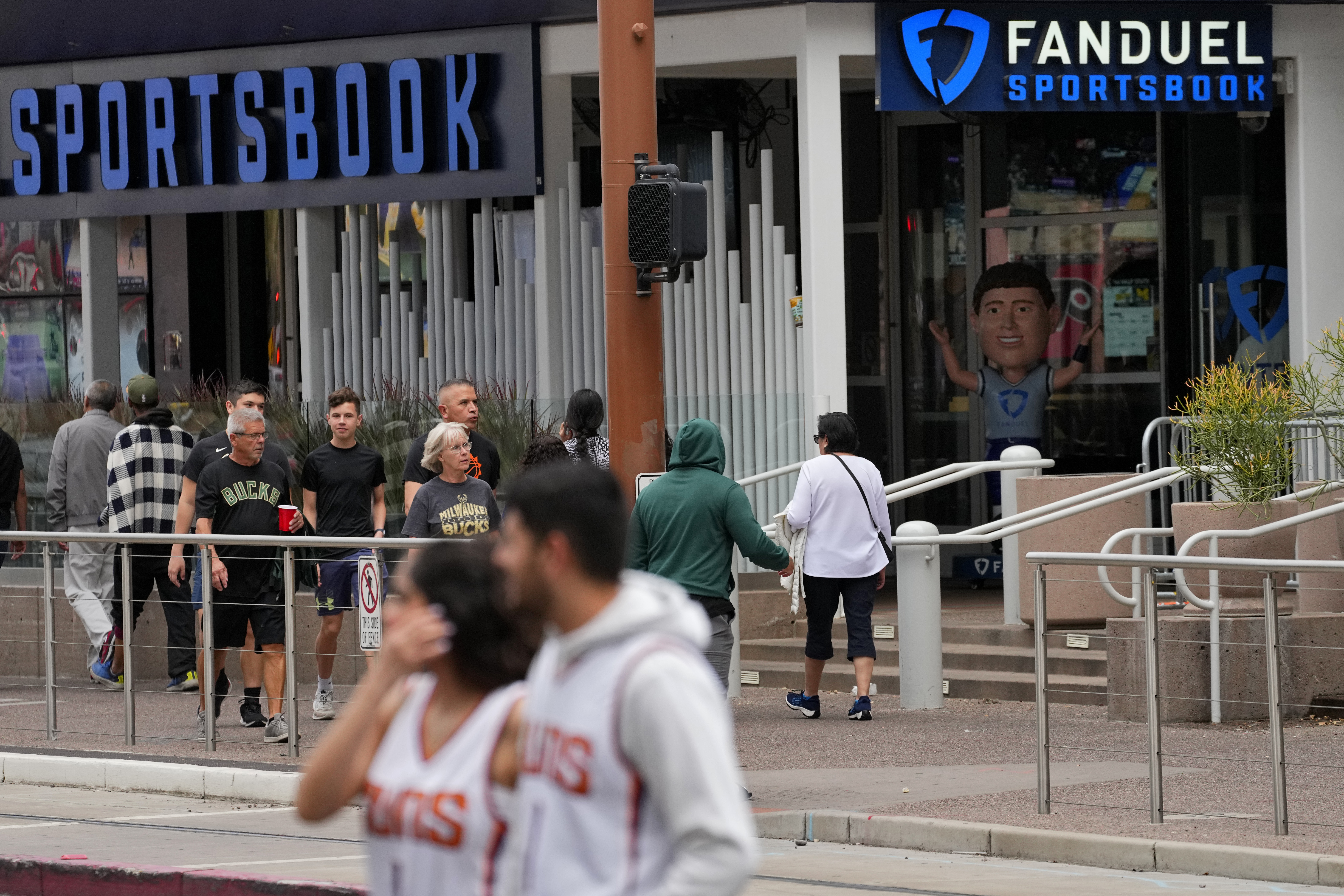 Fans walks past a sportsbook attached to the Footprint Center, Tuesday, March 14, 2023, in Phoenix. Major League Baseball — long the most gambling-averse of the U.S. leagues — now permits its players to be ambassadors for gambling companies. It’s the backdrop for an era of legal sports betting in the U.S. that’s brought in huge revenues but also has some experts sounding cautionary notes. 