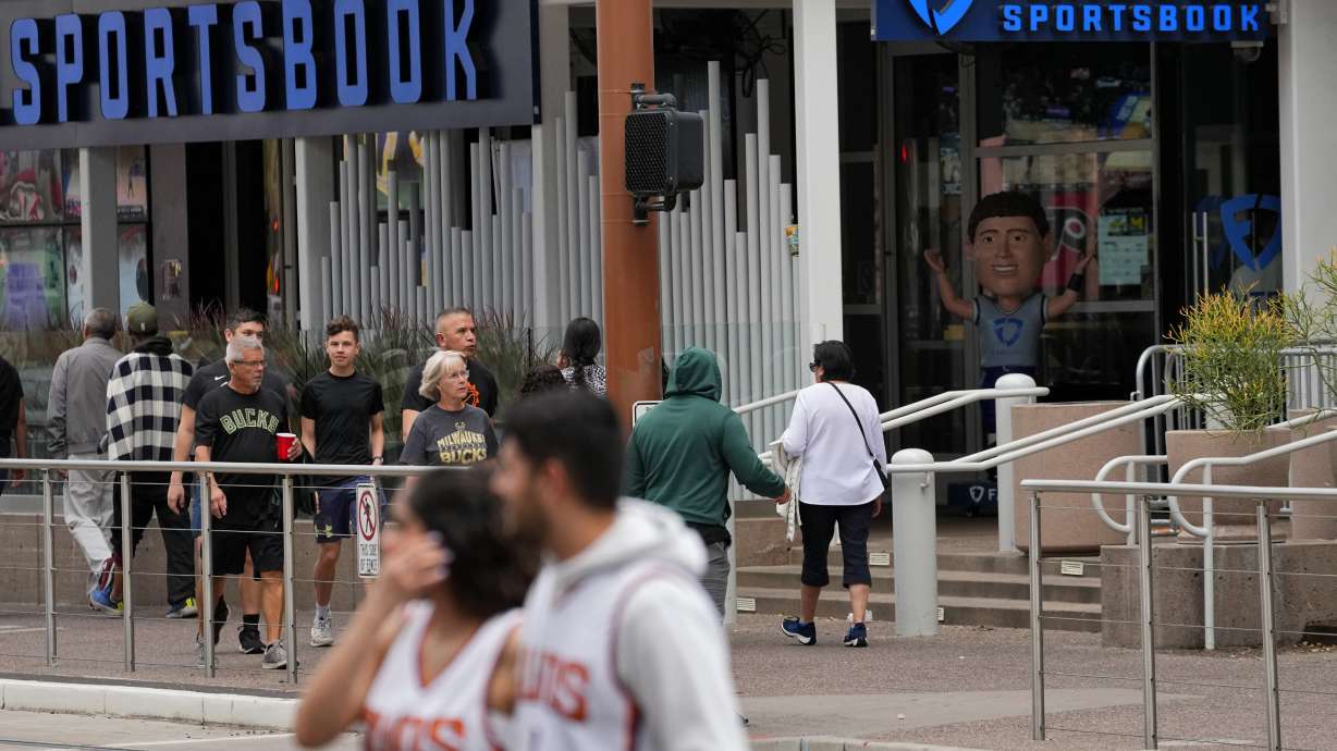 Fans walks past a sportsbook attached to the Footprint Center, Tuesday, March 14, 2023, in Phoenix. Major League Baseball — long the most gambling-averse of the U.S. leagues — now permits its players to be ambassadors for gambling companies. It’s the backdrop for an era of legal sports betting in the U.S. that’s brought in huge revenues but also has some experts sounding cautionary notes.