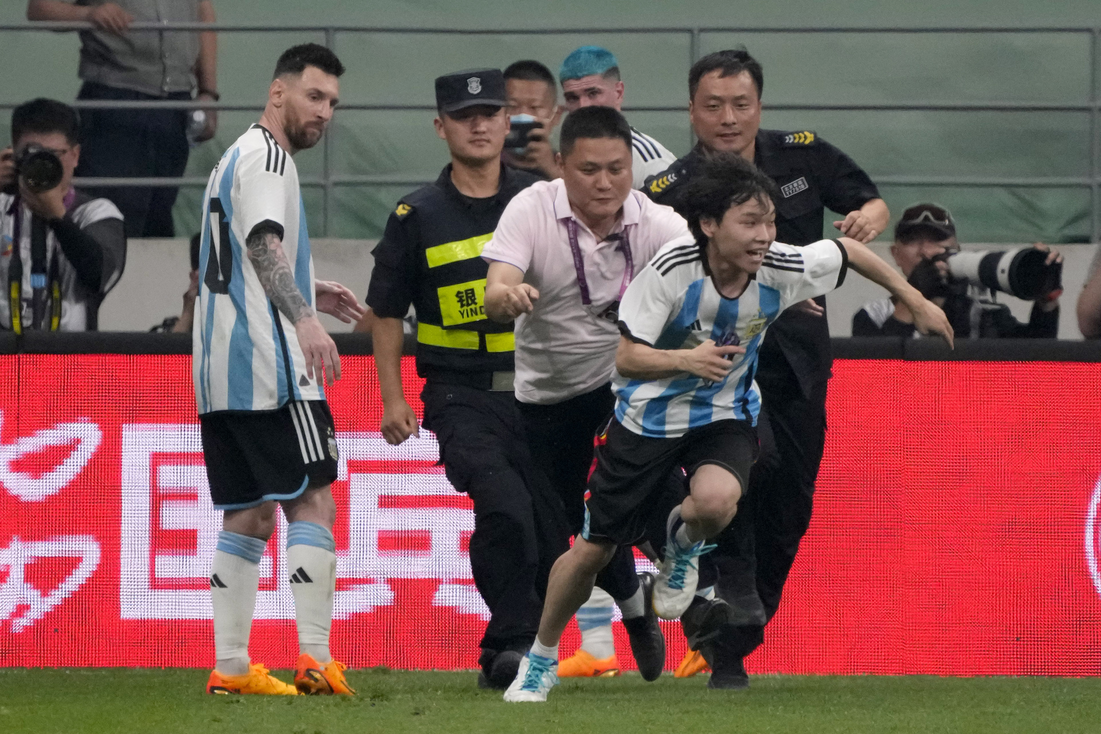 Argentina's Lionel Messi, left, watches as security officers pursue a fan during play on the field in their friendly soccer match at Workers' Stadium in Beijing, Thursday, June 15, 2023.