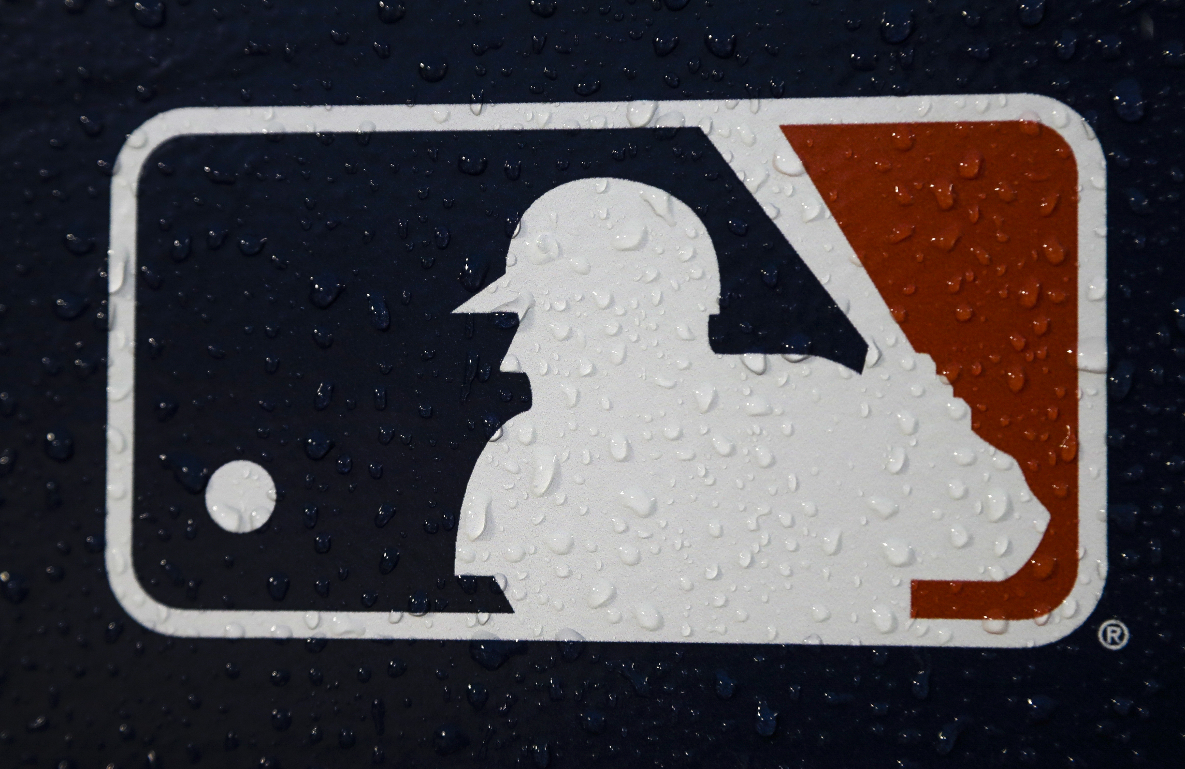 FILE - A rain-covered MLB logo is seen at Fenway Park before Game 1 of the World Series baseball game between the Boston Red Sox and the Los Angeles Dodgers, Oct. 23, 2018, in Boston. Seventeen former Major League Baseball scouts who say they were discriminated against because of their age sued the league, its teams and Commissioner Rob Manfred on Wednesday, June 21, 2023. 