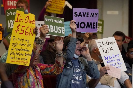People who support ending the eviction moratorium yell and hold up signs during a Oakland City Council special community and economic development committee at City Hall in Oakland, Calif., April 11.