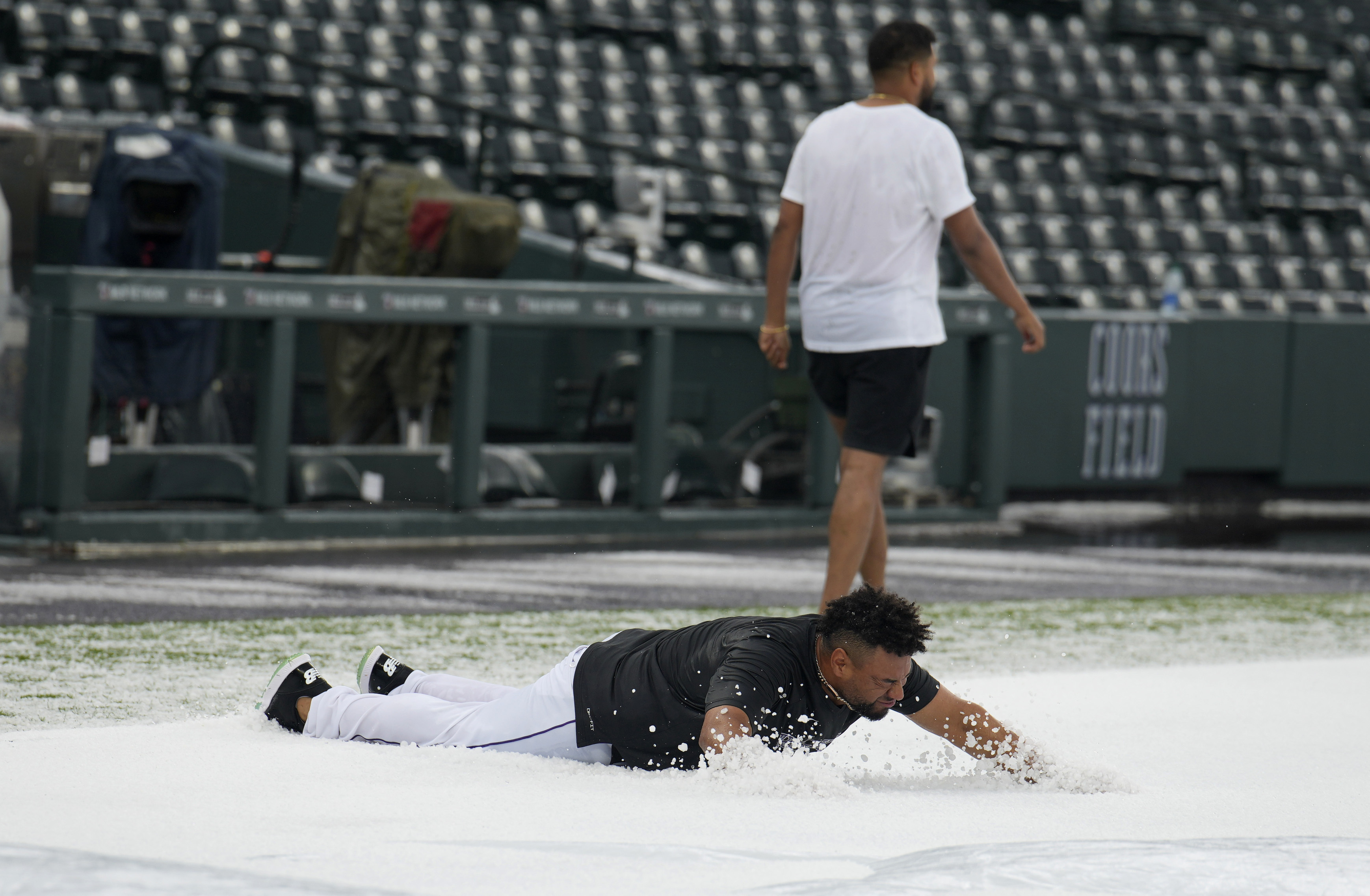 Colorado Rockies catcher Elias Diaz, front, dives onto a hail-covered tarpaulin after a summer storm packing heavy rain, high winds and large hail swept over Coors Field, Thursday, June 29, 2023, in Denver. Injured Rockies pitcher German Marquez, back, walks away. The Rockies were set to host the Los Angeles Dodgers, Thursday.