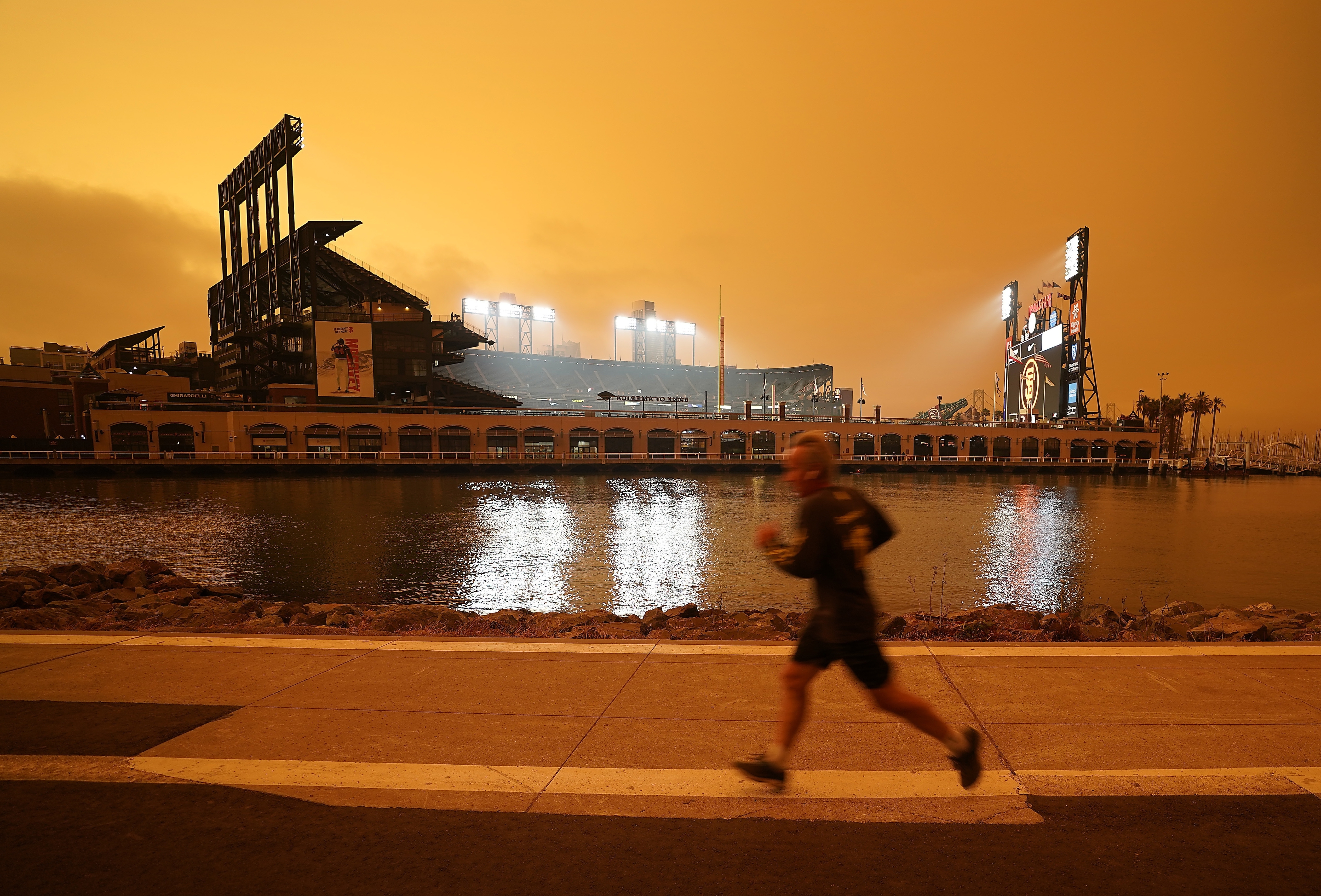 A jogger runs outside Oracle Park in San Francisco, under darkened skies from wildfire smoke on Sept. 9, 2020. As Earth's climate continues to change, ever fewer people are out of reach from the deadly fingers of wildfire smoke, scientists say. 