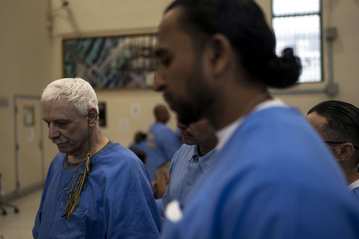 Prisoner-students Leroy Dehaven, left, with a tassel hanging from his ear, and Gerald Massey, foreground, wait to return to their cells after their graduation ceremony at Folsom State Prison in Folsom, Calif. on May 25, 2023.