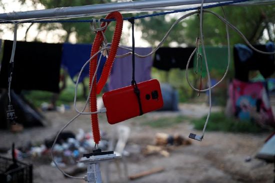 An asylum seeker hangs his cellphone on a rope while recharging the battery, while he waits to attempt to cross into the U.S. by an appointment through the Customs and Border Protection app, called CBP One, at a makeshift camp, in Matamoros, Mexico, June 21.