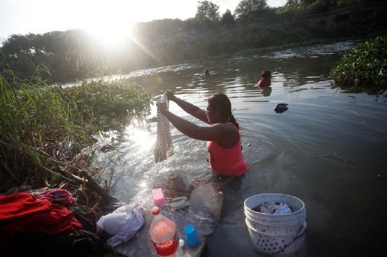 An asylum seeker washes her clothes in the Rio Grande river while she waits to attempt to cross into the U.S. by an appointment through the Customs and Border Protection app, called CBP One, at a makeshift camp, in Matamoros, Mexico, June 21.