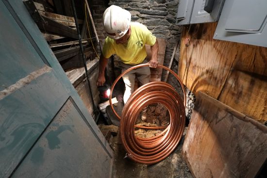 George Philbin, of Boyle & Fogarty Construction, works to feed a new copper residential water supply line, after removing a old lead residential water supply line, in the basement of a home where service was getting upgraded June 29 in Providence, R.I.