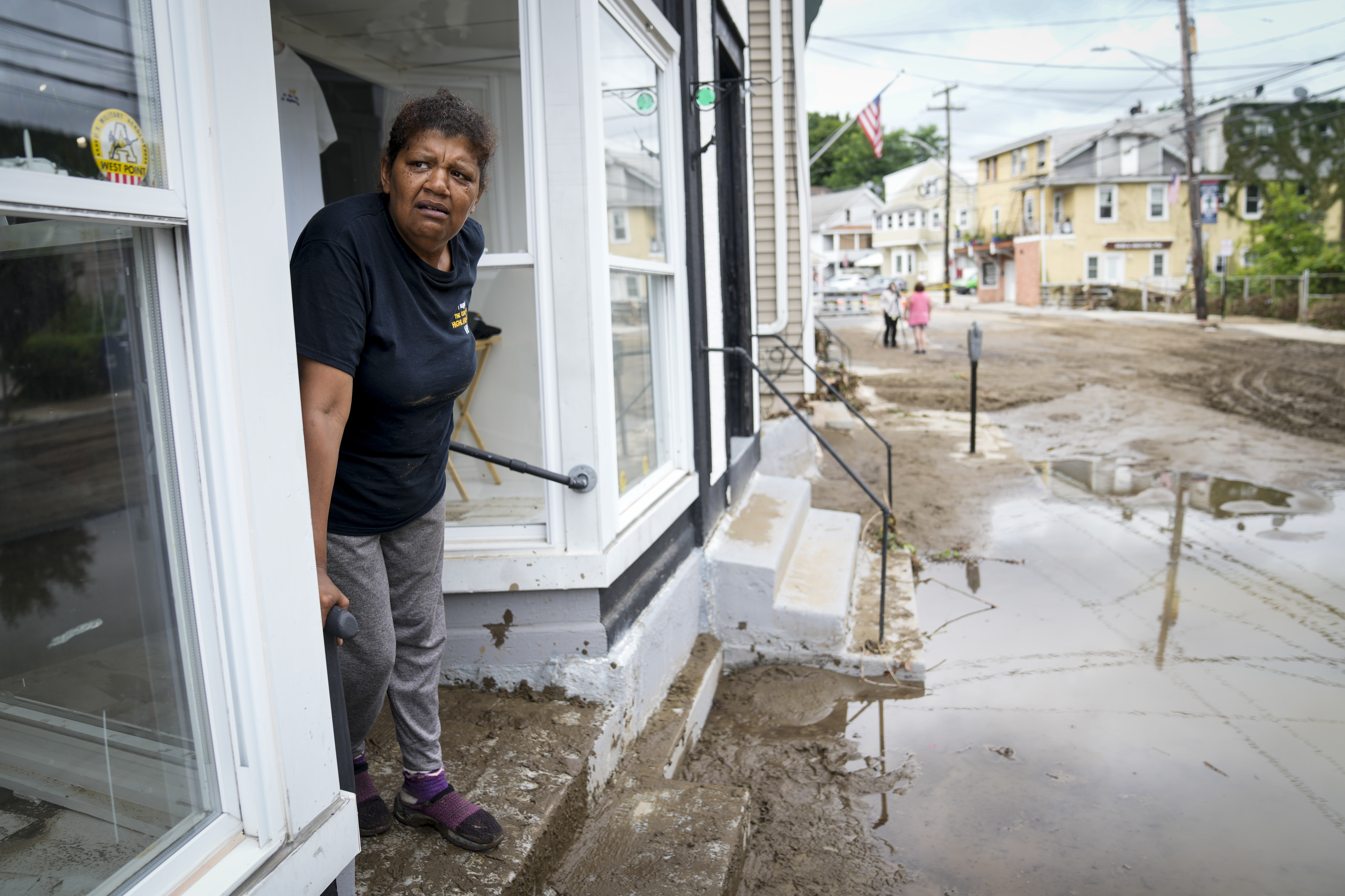 Kathy Eason, a worker at the Center for Highland Falls, stands on the storefront's stoop where she had been trapped by floodwaters the previous day, Monday, in Highland Falls, N.Y.