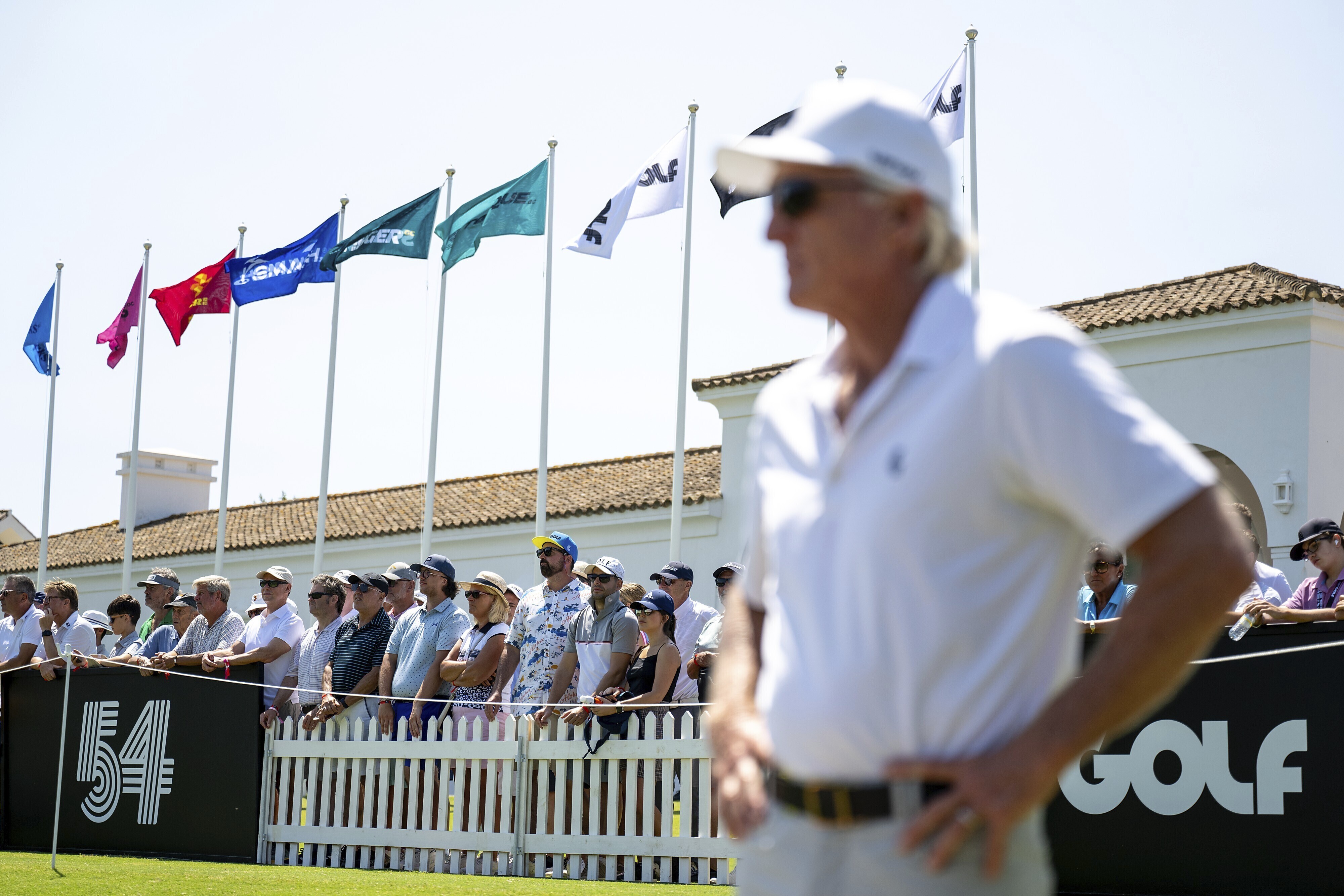 Fans watch as LIV Golf CEO Greg Norman looks on from the driving range before the first round of an LIV golf tournament at the Real Club Valderrama in San Roque, Spain, Friday, June 30, 2023. 