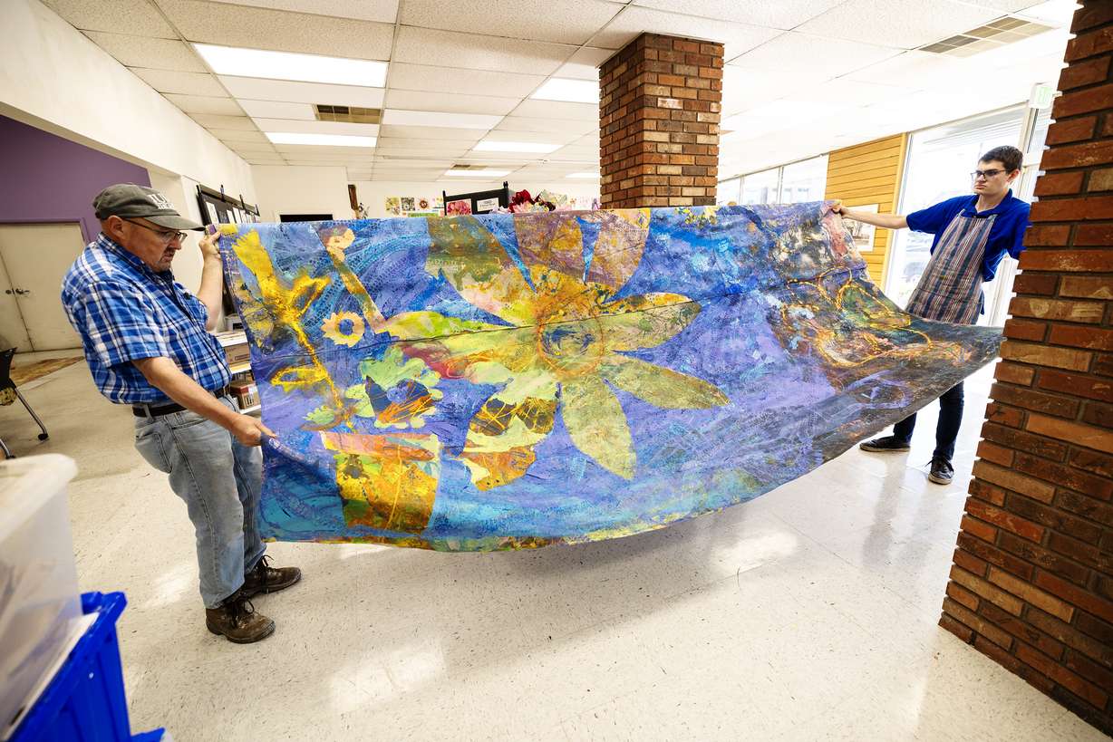 Michael Bingham, executive director of Jump the Moon, a nonprofit art studio and gallery organization in Logan, and Service Missionary Elder Crookston of The Church of Jesus Christ of Latter-day Saints, show a large painting by Kaya Eccles, an artist in Logan who uses a wheelchair to apply the paint, on Wednesday.