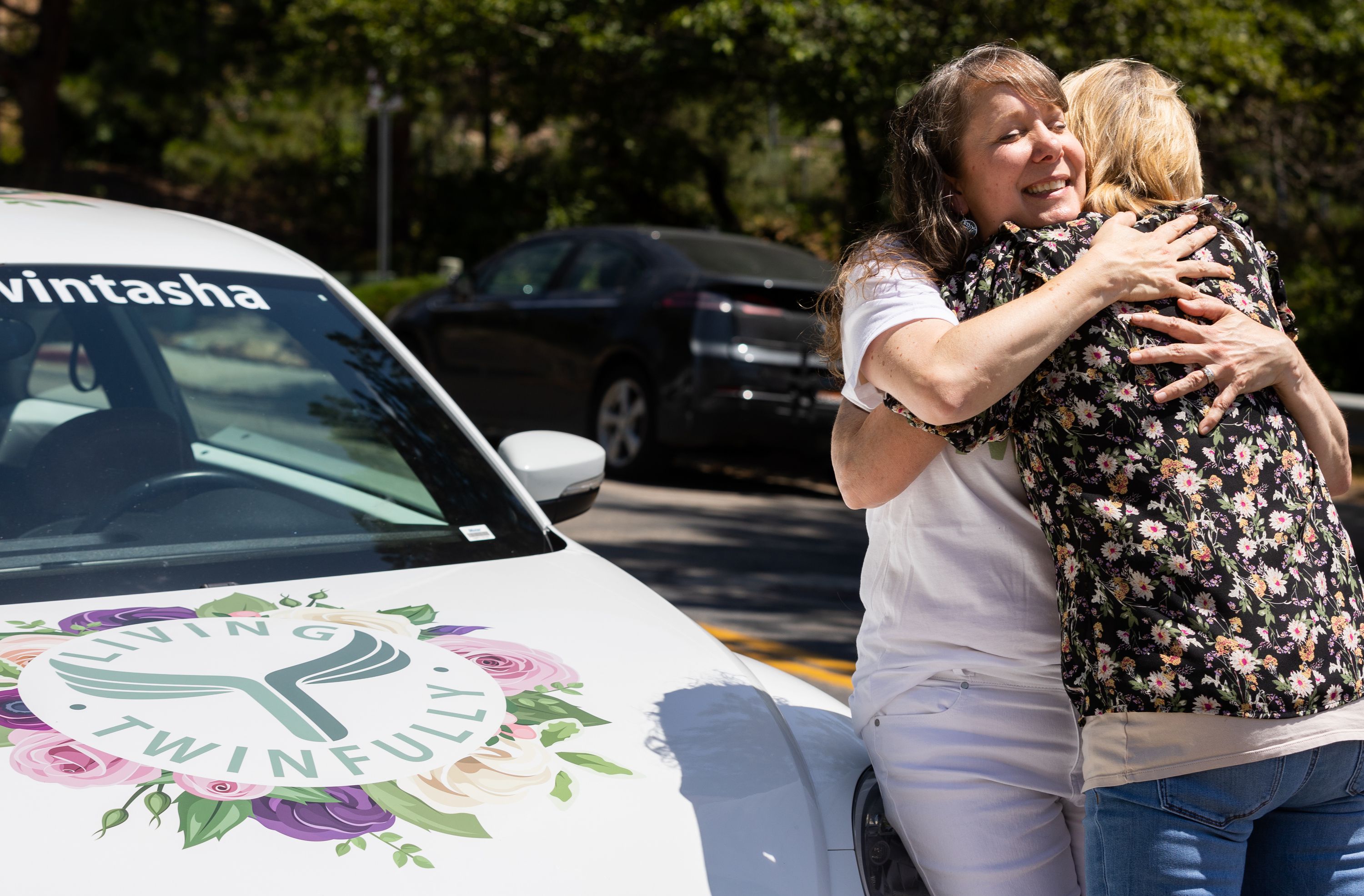 Left to right, Tasha Cram hugs Charla Haley next to the Hug Bug at the Presidential Club Condos in Salt Lake City on July 8. After losing her twin at age 4, Cram is on a journey to give 1,000 healing hugs to twins across the U.S.