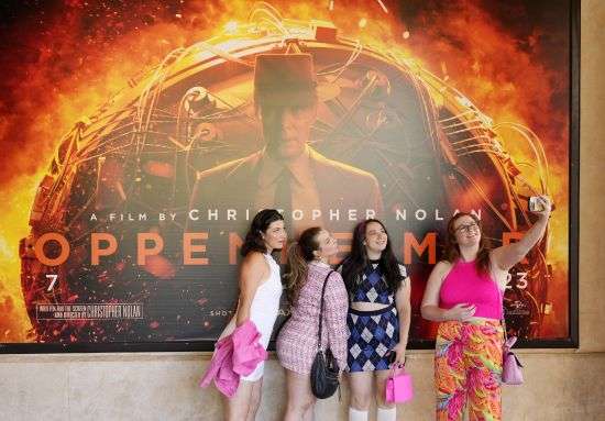 From left, Gabrielle Roitman, Kayla Seffing, Maddy Hiller and Casey Myer take a selfie in front of an "Oppenheimer" movie poster before they attended an advance screening of "Barbie," Thursday, at AMC The Grove 14 theaters in Los Angeles.