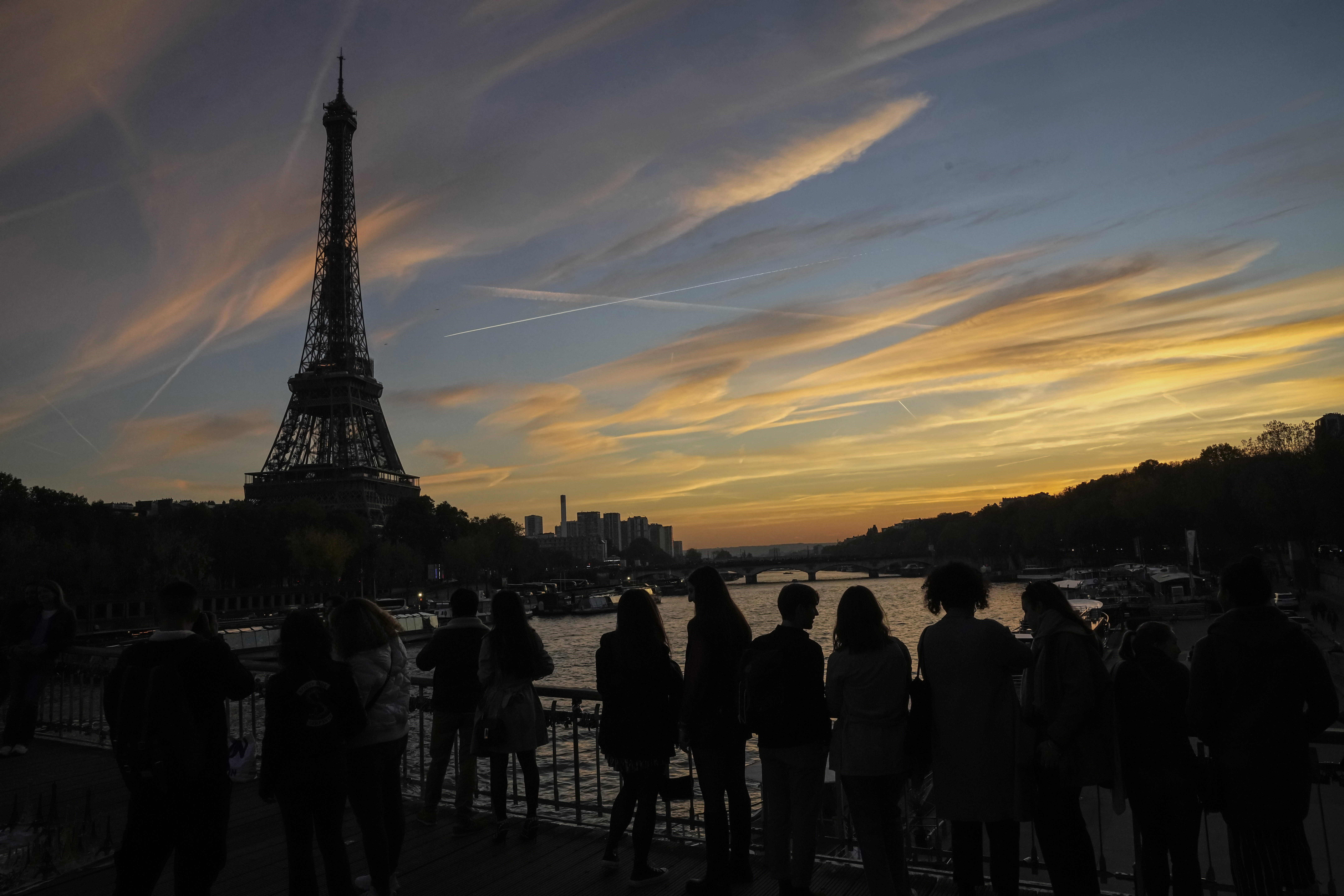 People watch the skyline as the cross the Debilly bridge near the Eiffel Tower during sunset in Paris, Saturday, Nov. 12, 2022. Paris is on track to host millions of visitors and successfully stage 32 sporting events next year when the 2024 Olympics open on July 26. That's a welcome return to business as usual for the first post-pandemic Olympics. 
