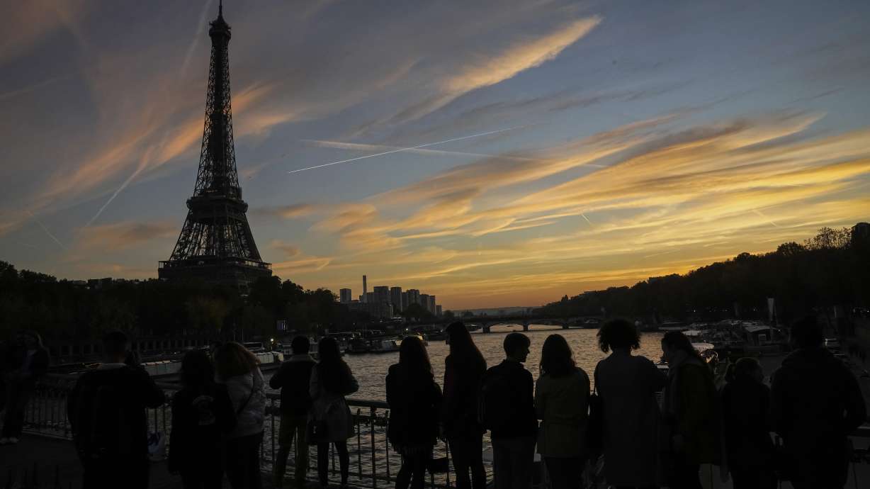 People watch the skyline as the cross the Debilly bridge near the Eiffel Tower during sunset in Paris, Saturday, Nov. 12, 2022. Paris is on track to host millions of visitors and successfully stage 32 sporting events next year when the 2024 Olympics open on July 26. That's a welcome return to business as usual for the first post-pandemic Olympics.