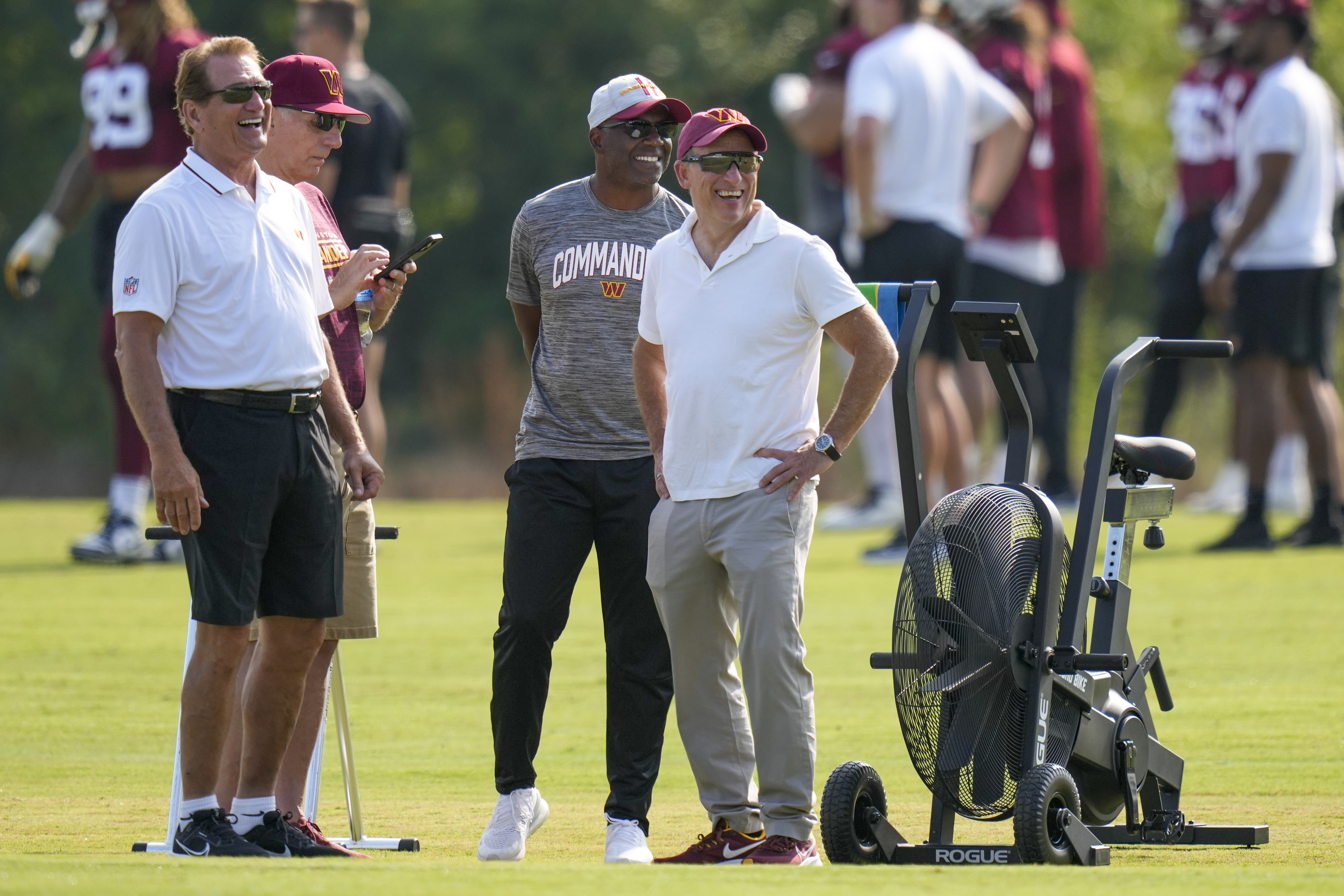 Washington Commanders owner Josh Harris, right, laughs with Joe Theismann, left, Mitchell Rales, and others, during NFL football practice at the team's training facility, Wednesday, July 26, 2023 in Ashburn, Va.