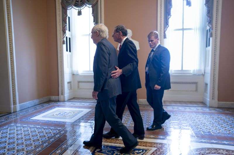 Senate Minority Leader Mitch McConnell, R-Ky., left, is assisted by Sen. John Barrasso, R-Wyo., second from right, and a Capitol Police officer after the 81-year-old GOP leader froze at the microphones as he arrived for a news conference at the Capitol in Washington, Wednesday. McConnell went to his office for a few minutes and returned to speak with reporters.