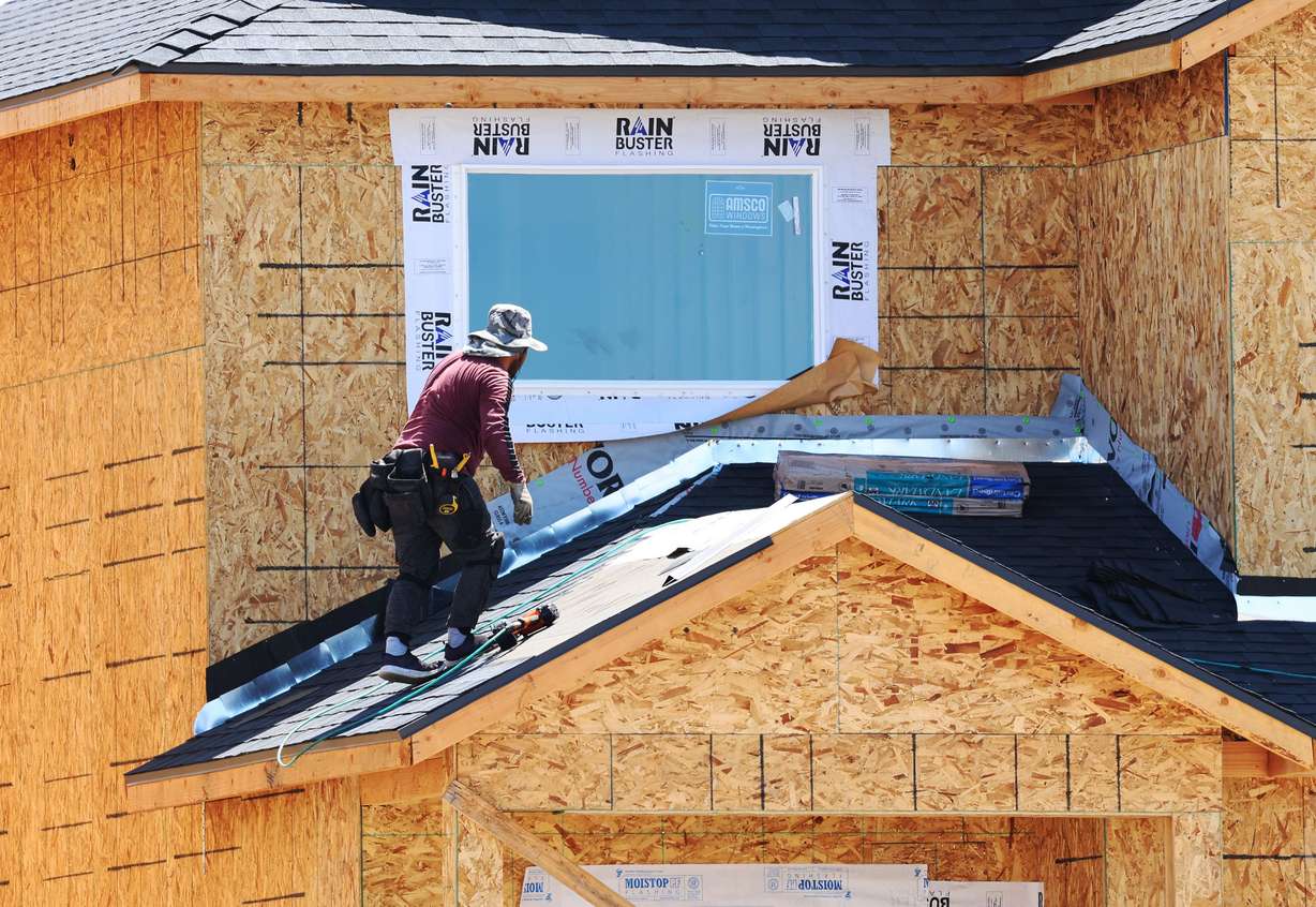 A roofer lays shingles at Ivory Homes’ Gabler’s Grove development in Magna on Tuesday.