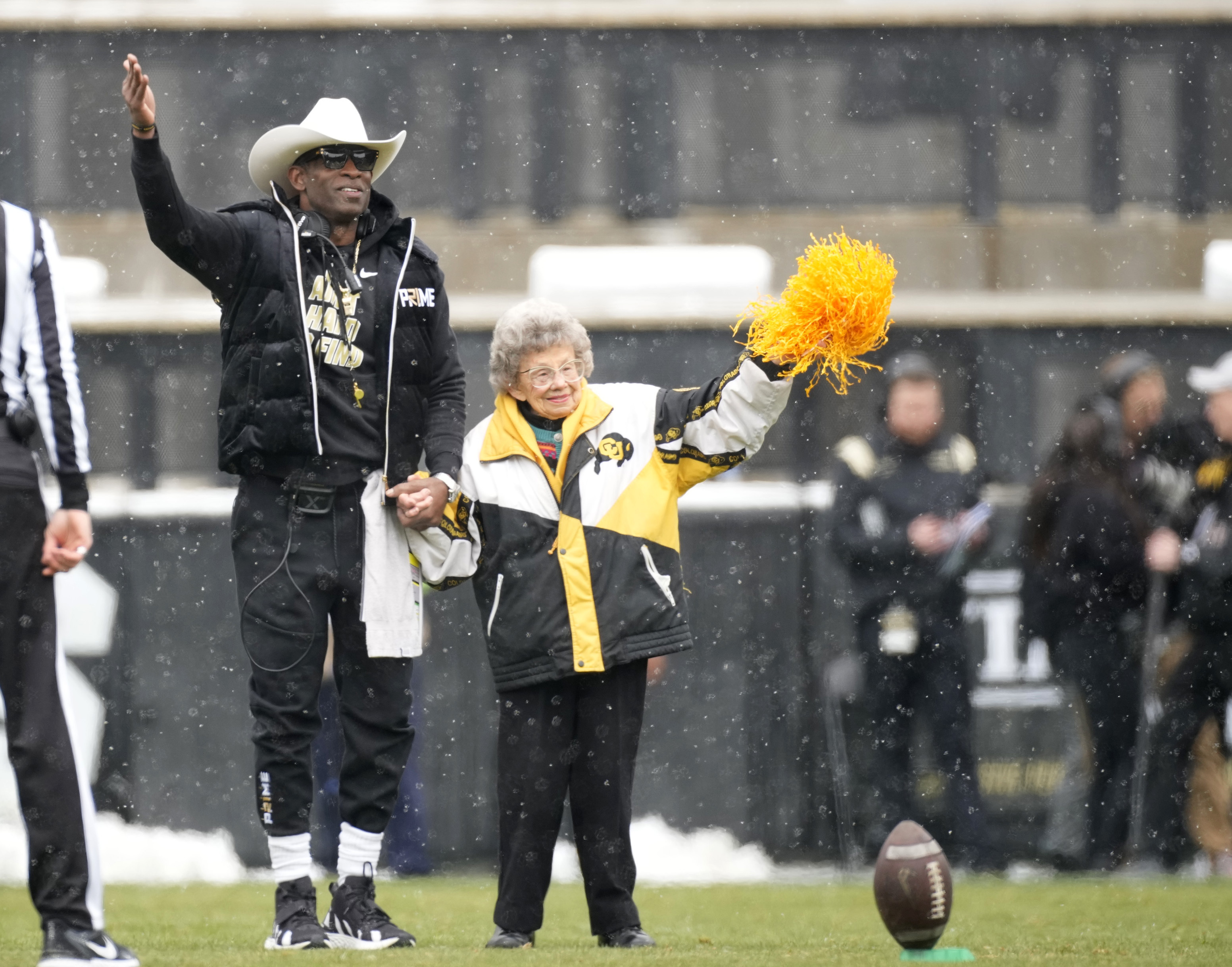 FILE - Colorado coach Deion Sanders, left, leads longtime supporter Peggy Coppom to kick the football before the team's spring practice NCAA college football game April 22, 2023, in Boulder, Colo. Coppom, 98, said she's excited about Colorado's return to the Big 12 in 2024. She has attended Colorado football games since 1940. 