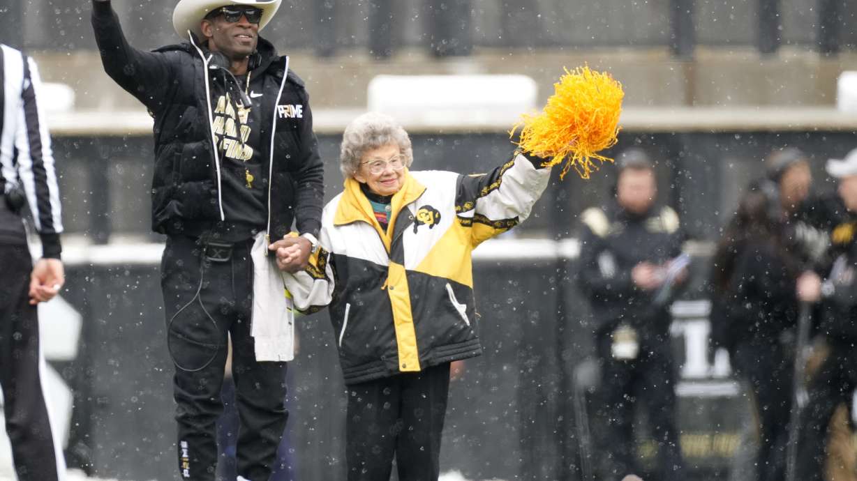 FILE - Colorado coach Deion Sanders, left, leads longtime supporter Peggy Coppom to kick the football before the team's spring practice NCAA college football game April 22, 2023, in Boulder, Colo. Coppom, 98, said she's excited about Colorado's return to the Big 12 in 2024. She has attended Colorado football games since 1940.