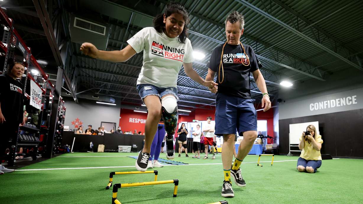 Jennifer Lozano is steadied by Mark Lange from Shriners as she jumps over obstacles with her new recreational prosthesis as part of the Running is a Right program on Saturday.