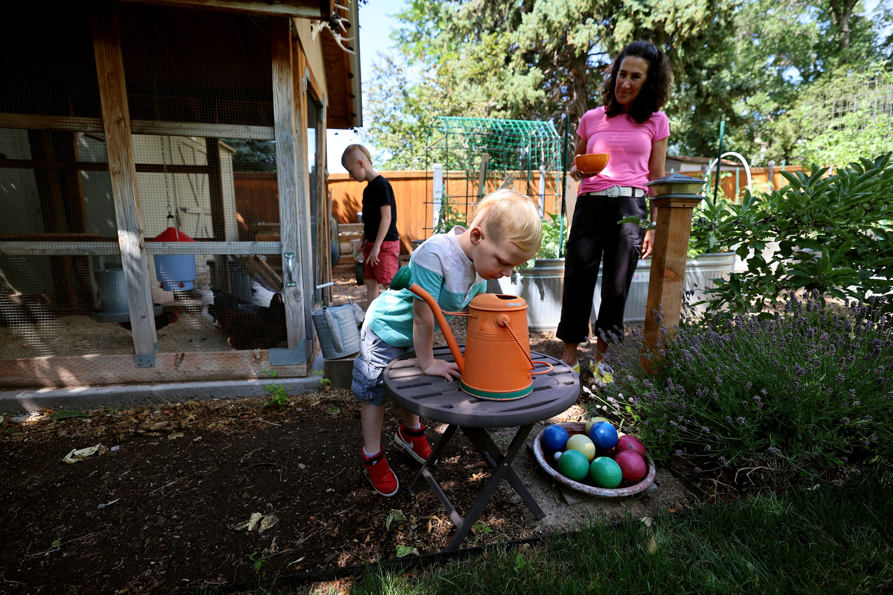 Dr. Bonnie Feola watches as Ellis looks down into a watering can in her garden in Salt Lake City on July 26. Feola works with kids and parents on learning about eating healthy and how to prepare food.