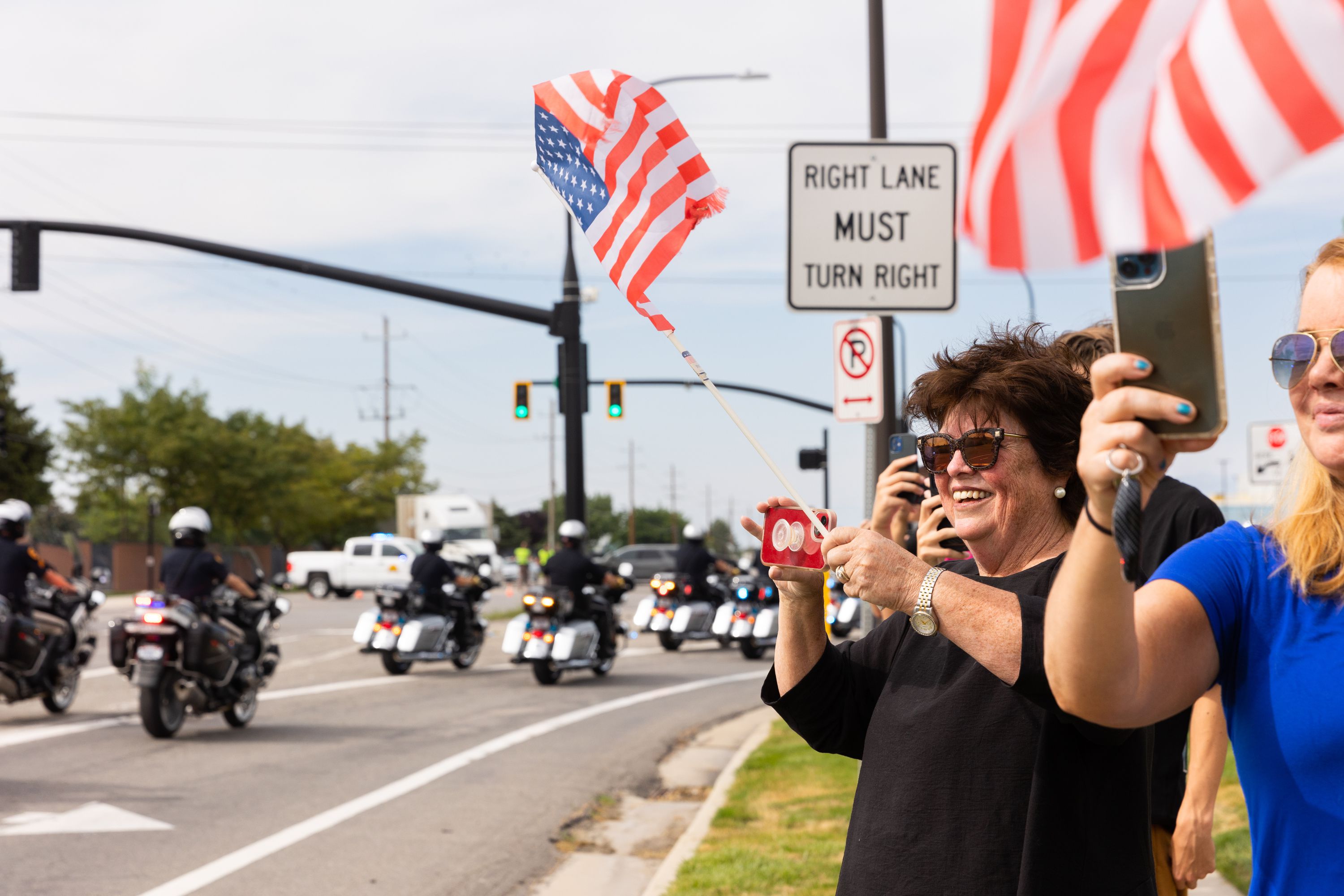 Kathy Stidham waves her American flag as the presidential motorcade drives out of the Roland R. Wright Air National Guard Base in Salt Lake City on Wednesday. The possibility of seeing President Joe Biden whiz by had about 100 people lined up to await the president's motorcade.
