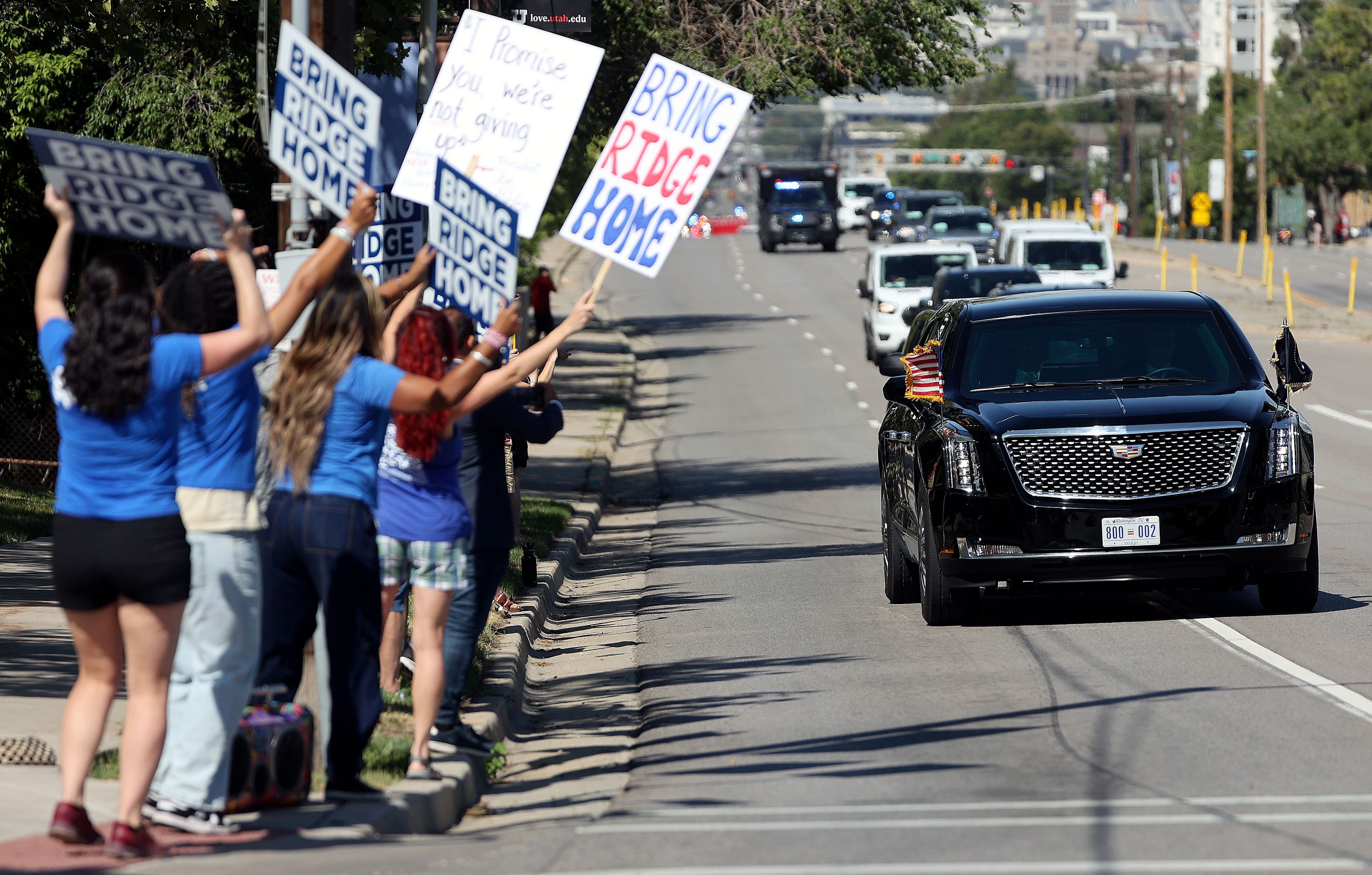 People hold “Bring Ridge Home” signs as a motorcade escorts President Joe Biden to the George E. Wahlen Department of Veterans Affairs Medical Center, where he delivered remarks, in Salt Lake City on Thursday.