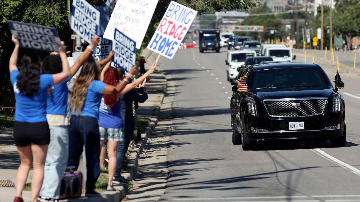 People hold “Bring Ridge Home” signs as a motorcade escorts President Joe Biden to the George E. Wahlen Department of Veterans Affairs Medical Center, where he delivered remarks, in Salt Lake City on Thursday.