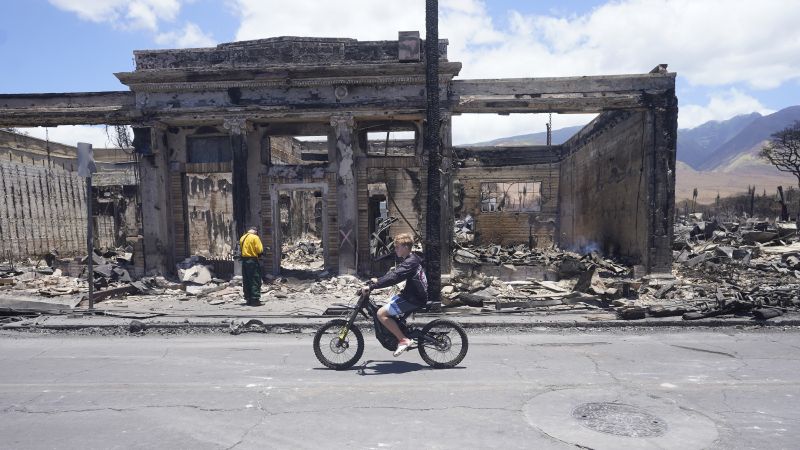 A boy rides along Main Street past wildfire damage on Aug. 11 in Lahaina, Hawaii.