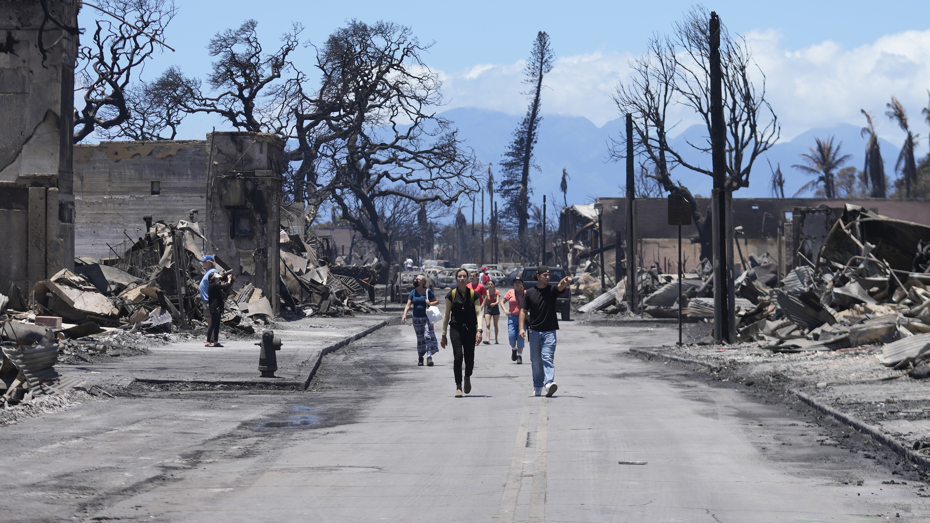 People walk along Main Street past wildfire damage on Friday, in Lahaina, Hawaii.
