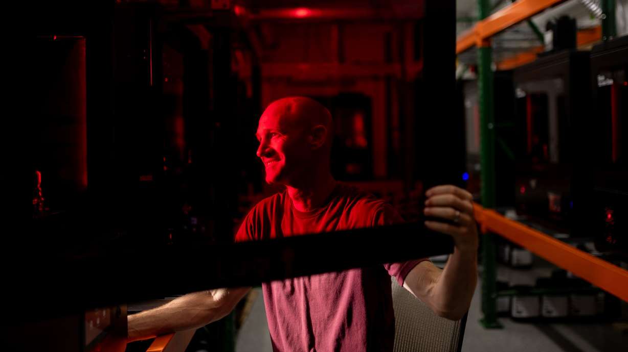 Spencer Loveless, CEO of Merit3D, an additive manufacturing company in Price, poses for a photo seen through the red-tinted door of one of the company’s LCD resin printers, which are a type of 3D printers, on Thursday.