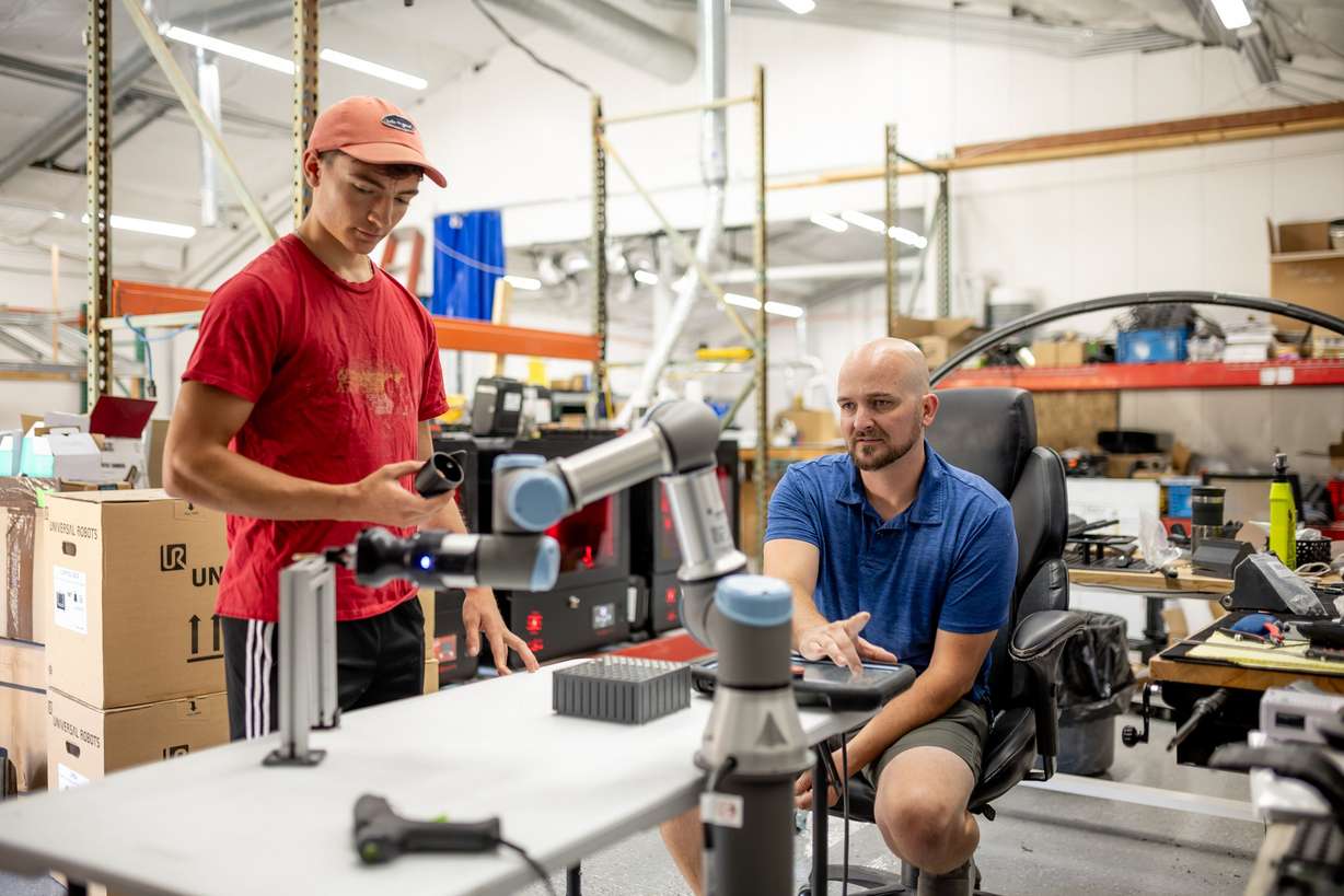Wesley Murray and Jason Marshall work with a robotic arm used for assembling products at Merit3D in Price on Thursday.
