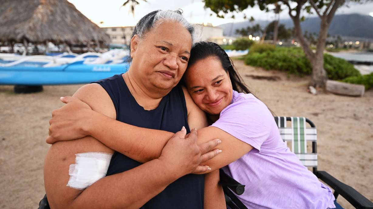 Noni Mirkovich and her daughter, Lani Williams, hug after doing an interview on Thursday, Aug. 17, 2023, talking about their experience of being forced into the ocean to survive the flames in Lahaina, Hawaii. The two and several others had to stay in the water for hours as the fire raged on shore. Response to the Maui fire that destroyed a large portion of the town of Lahaina continue to come in from neighboring islands and the mainland.