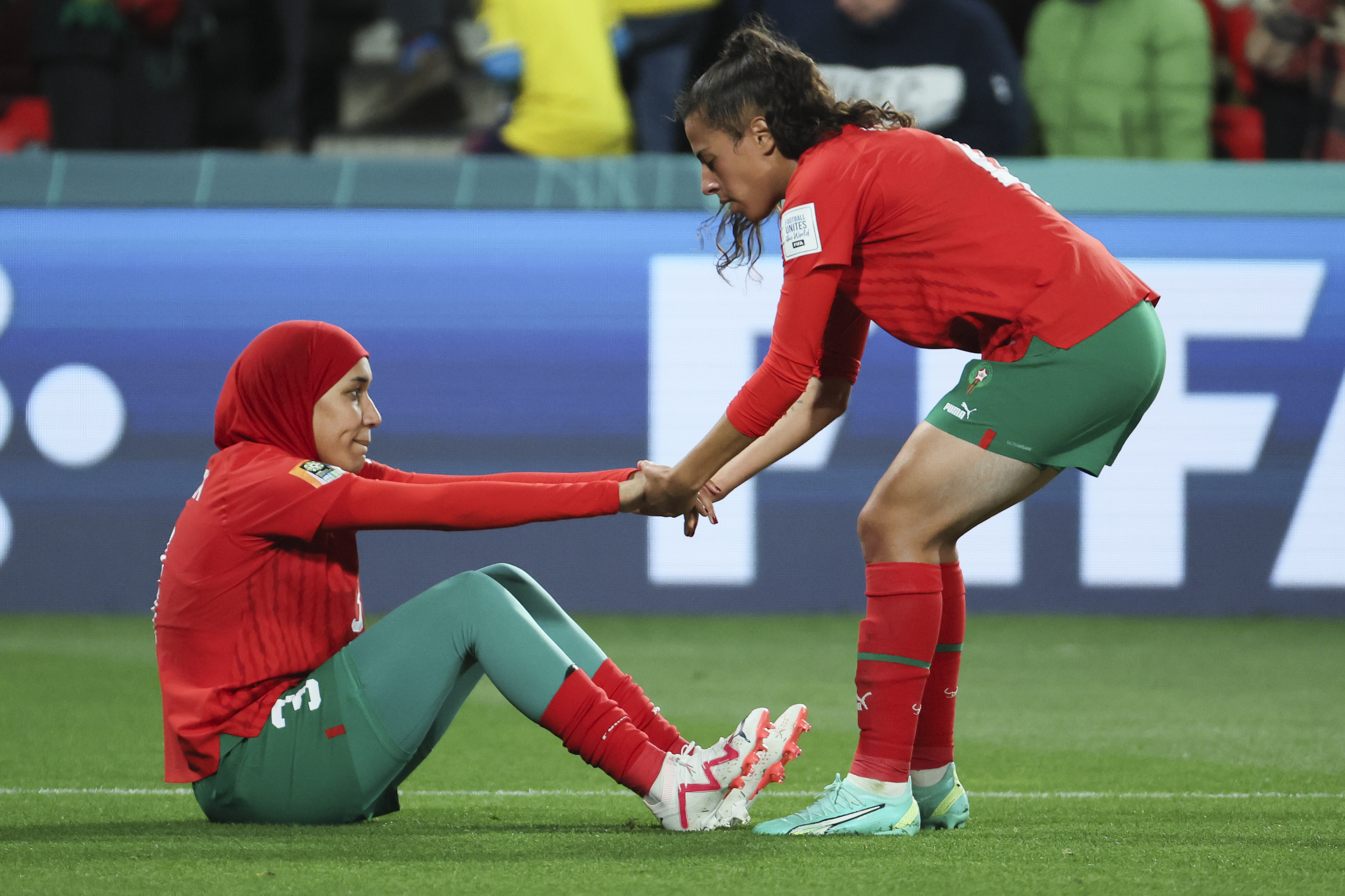Morocco's Nouhaila Benzina, left, is helped to her feet by teammate Sarah Kassi following the Women's World Cup round of 16 soccer match between France and Morocco in Adelaide, Australia, Tuesday, Aug. 8, 2023.