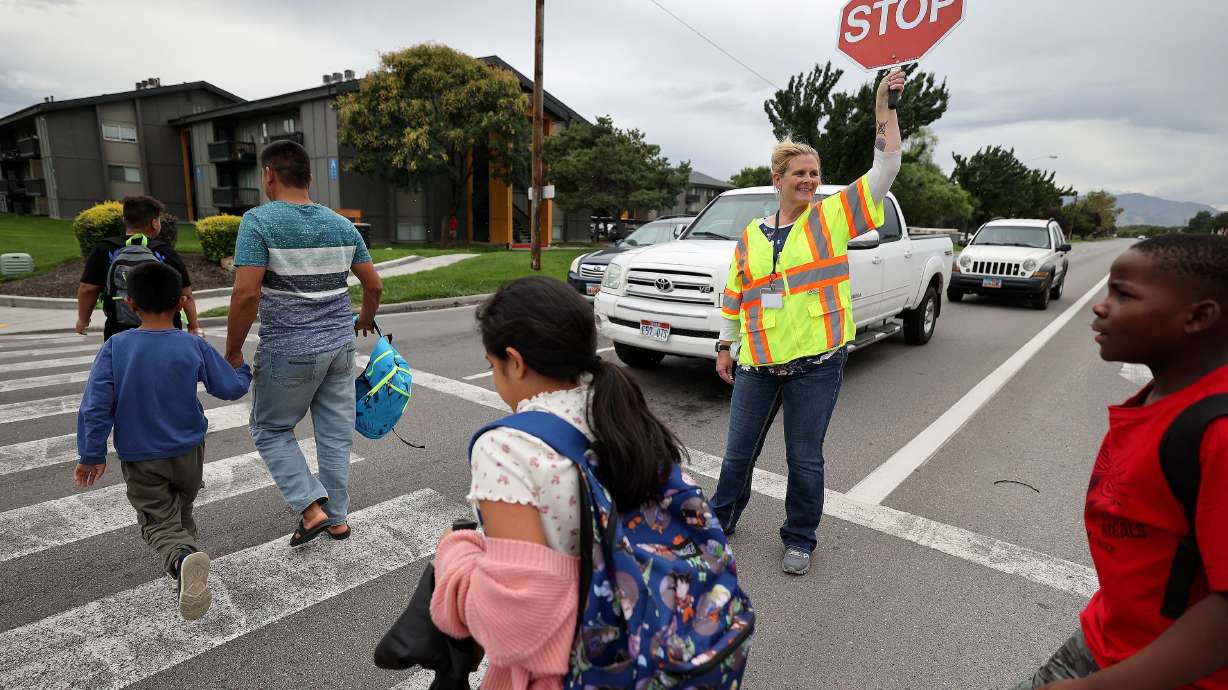 Unified police crossing guard April McCoy escorts people across 3900 South at 700 West on the border of South Salt Lake and Millcreek on Monday. Salt Lake City is looking to fill vacant crossing guard positions and is offering $17 an hour plus a $250 signing bonus.